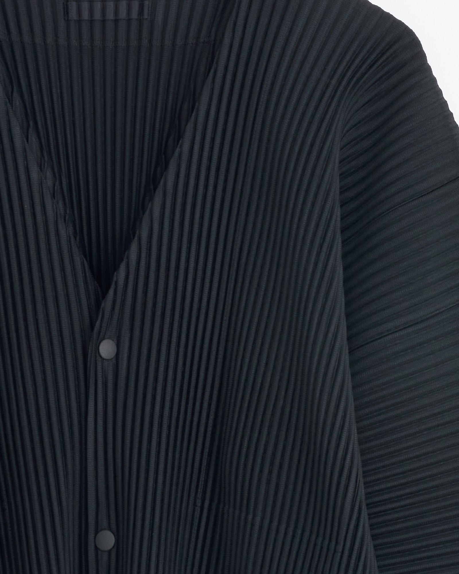 Close-up of the MC Oct Cardigan in Black by Homme Plissé Issey Miyake, featuring pleated fabric, V-neck, and snap buttons. For fit or sizing questions, reach out to our online chat for personalized help.