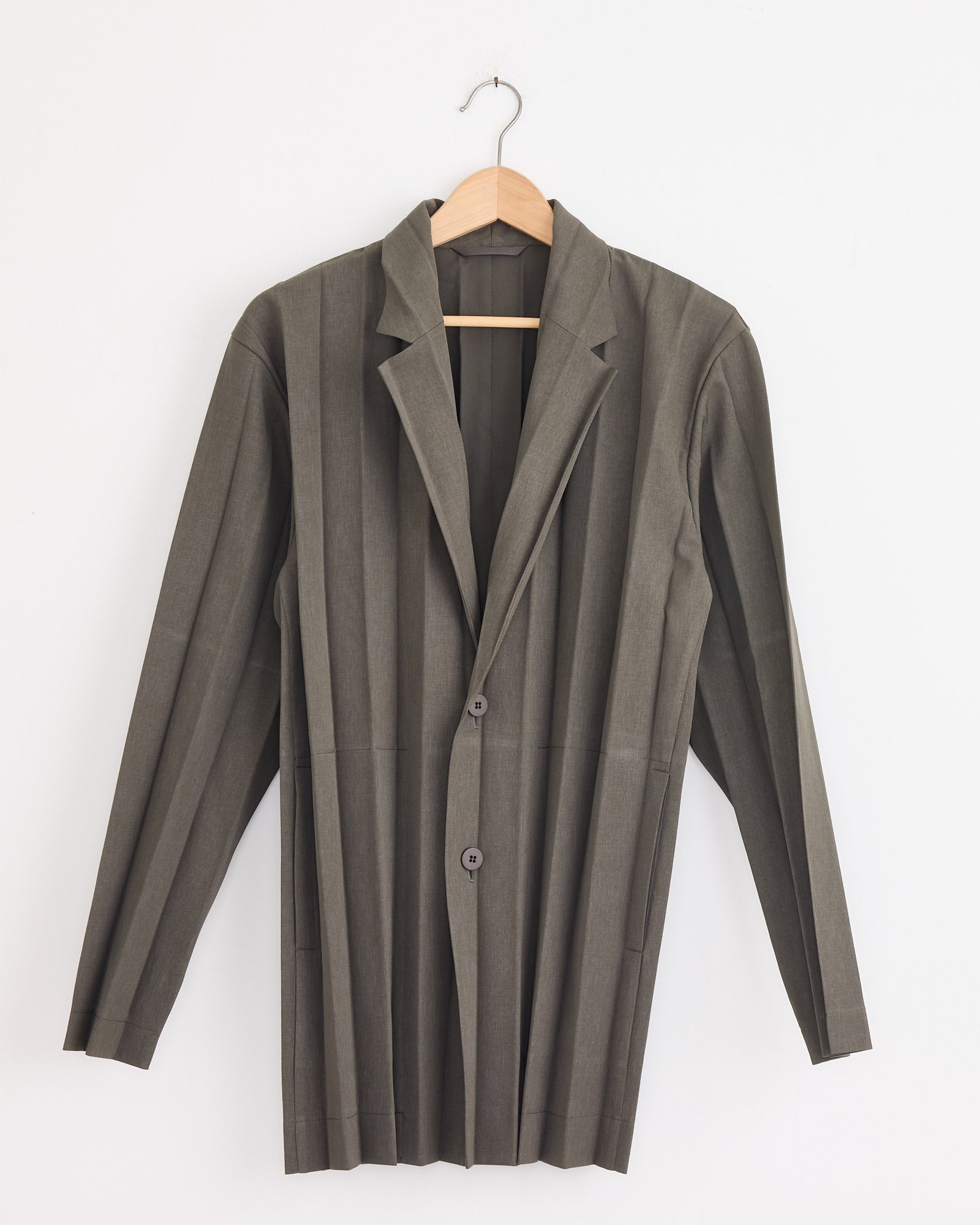 A model wears the Edge Ensemble Blazer in Khaki by Homme Plissé Issey Miyake, showcasing the brand’s signature accordion pleats.
