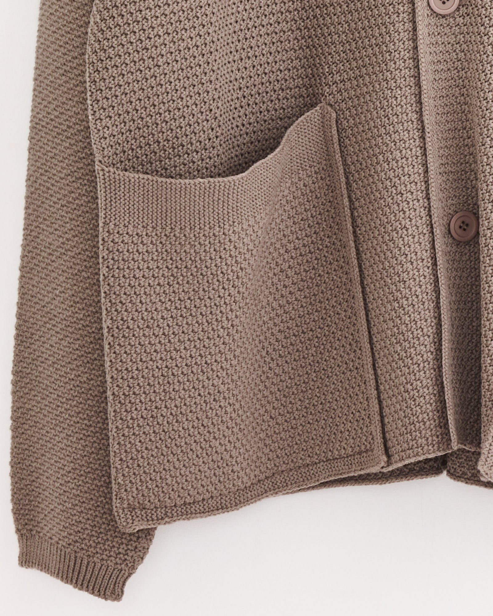 A close-up of the Rustic Knit Cardigan in Greige by Homme Plissé Issey Miyake, showcasing its textured pattern, large front pocket, brown buttons, and ribbed cuffs—ideal for perfect sizing help via online chat.