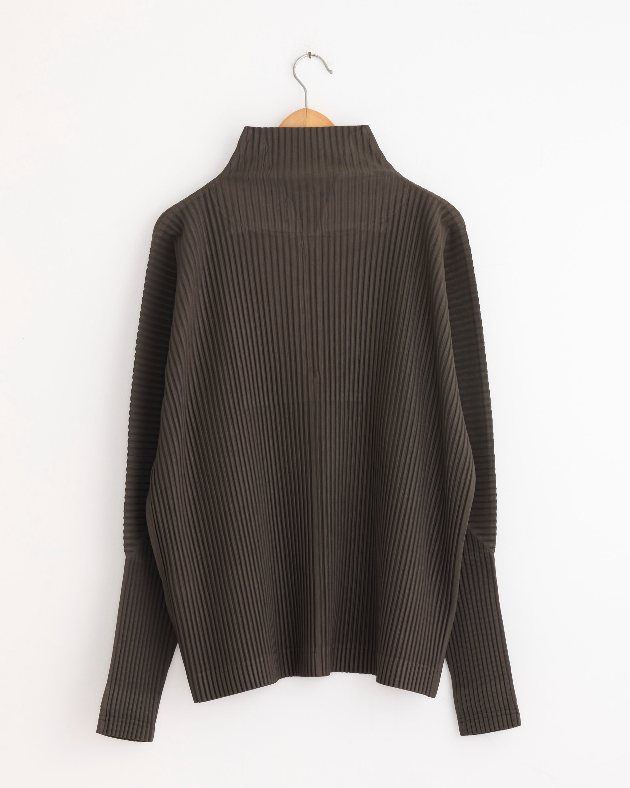 The MC Nov Jacket in Mudstone Grey by Homme Plissé Issey Miyake hangs on a wooden hanger against a white wall, back view visible with high collar and vertical texture. For sizing or fit help, use our online chat.