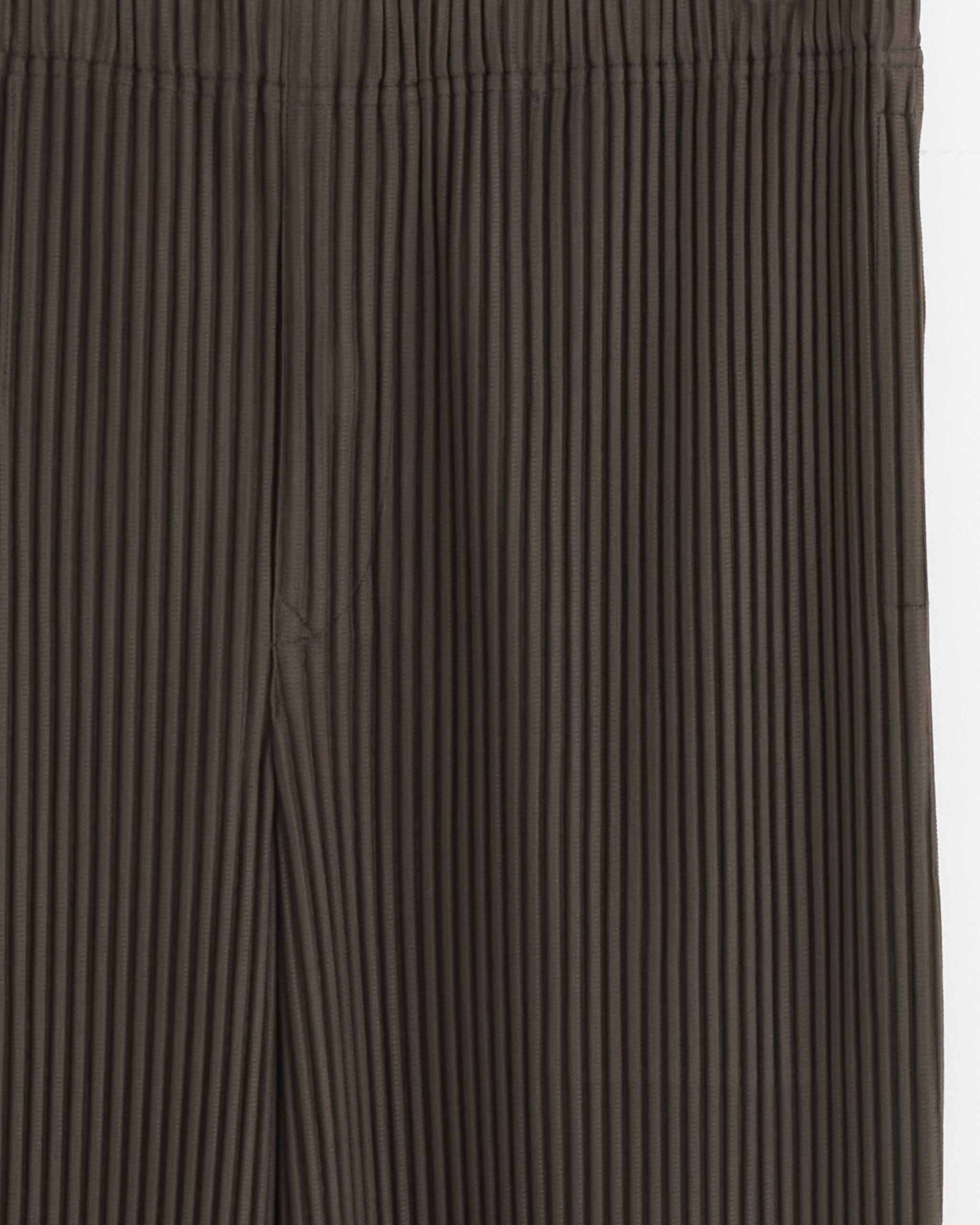Close-up of the MC Nov Pant in Mudstone Grey by Homme Plissé Issey Miyake, featuring quick-drying pleated polyester, an elastic waistband, and signature textured stitching.