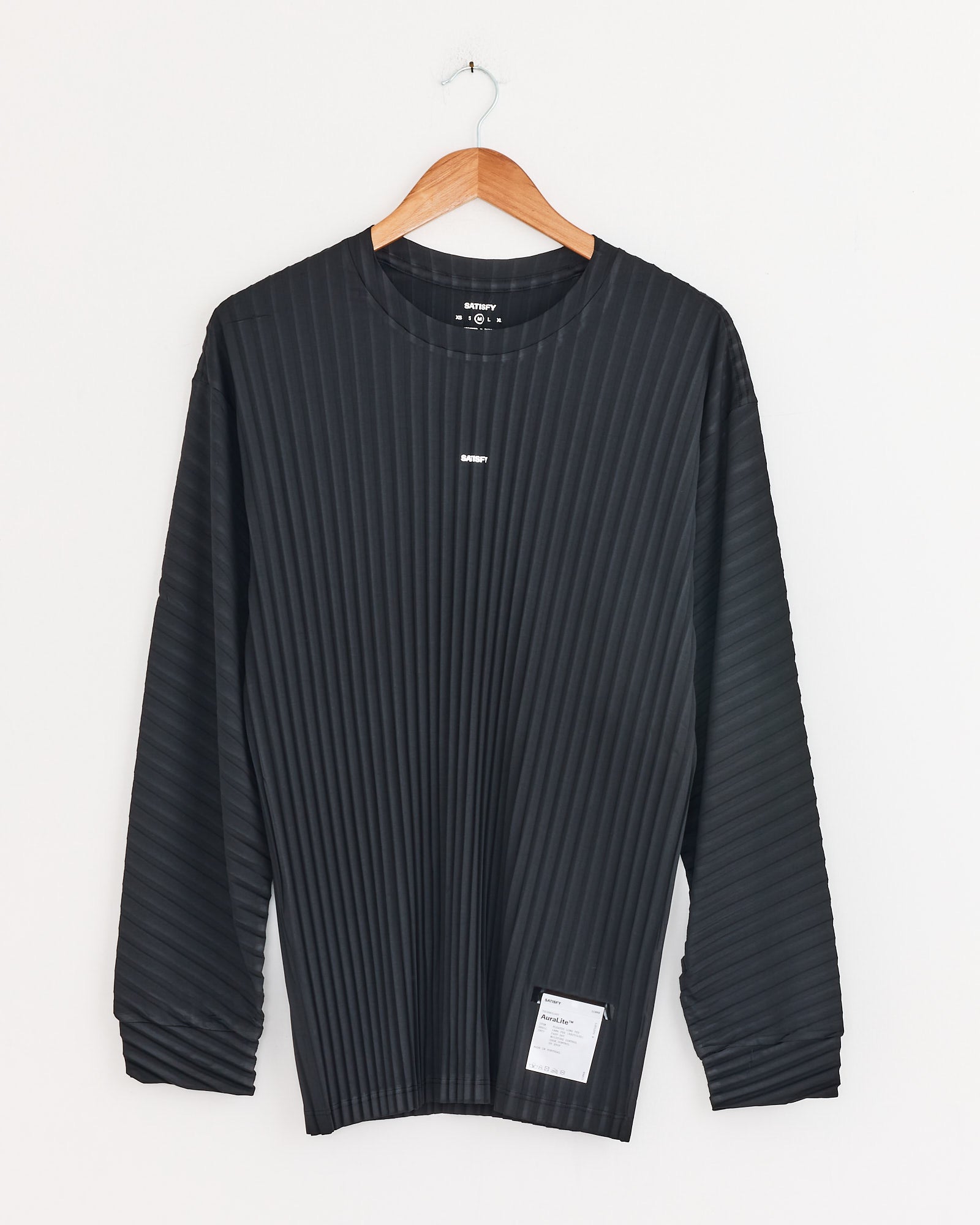 The Satisfy Running AuraLite Pleated Long Sleeve T-Shirt in Black, made from recycled micro jersey for moisture and odor control, features subtle vertical stripes, a small white label, and a centered chest logo.