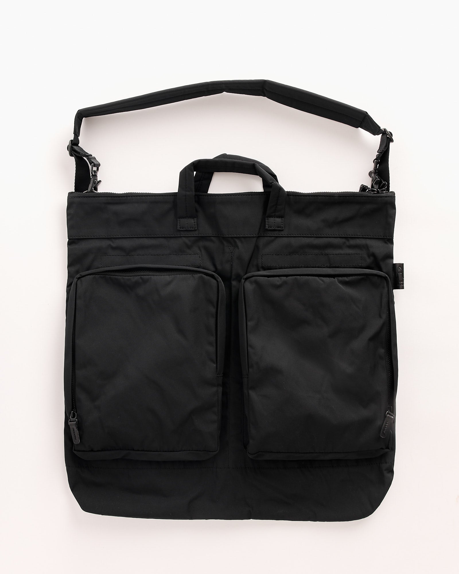 The Amiacalva Gabardine Helmet Bag in Black is a nylon tote with two large front zippered pockets, double top handles, and a detachable padded shoulder strap, shown on a plain white background. For fit questions, contact us via online chat.