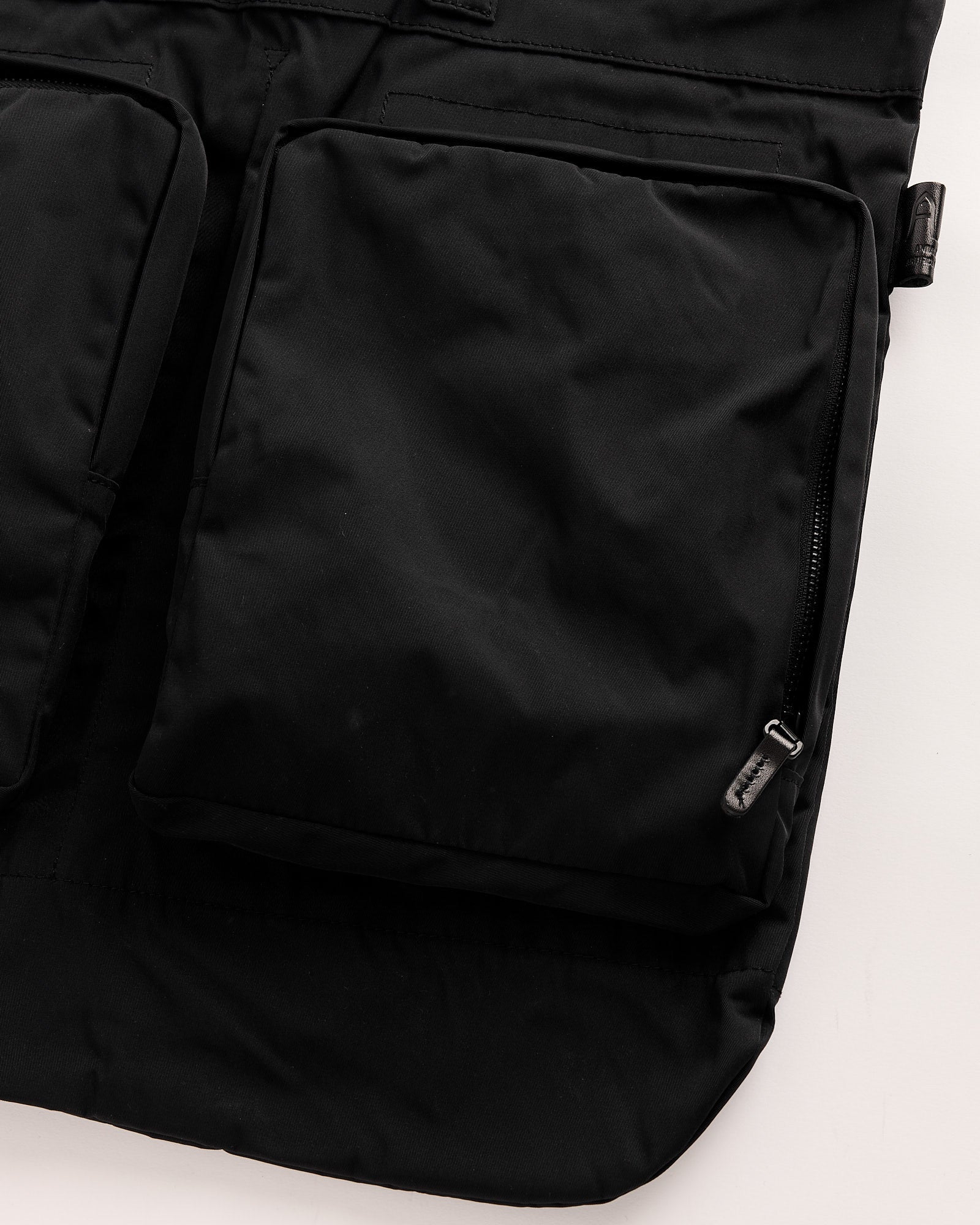 Close-up of the Amiacalva Gabardine Helmet Bag in black, featuring two large square zippered pockets and a smooth, minimal design on a light background. For fit or sizing inquiries, contact us via online chat.