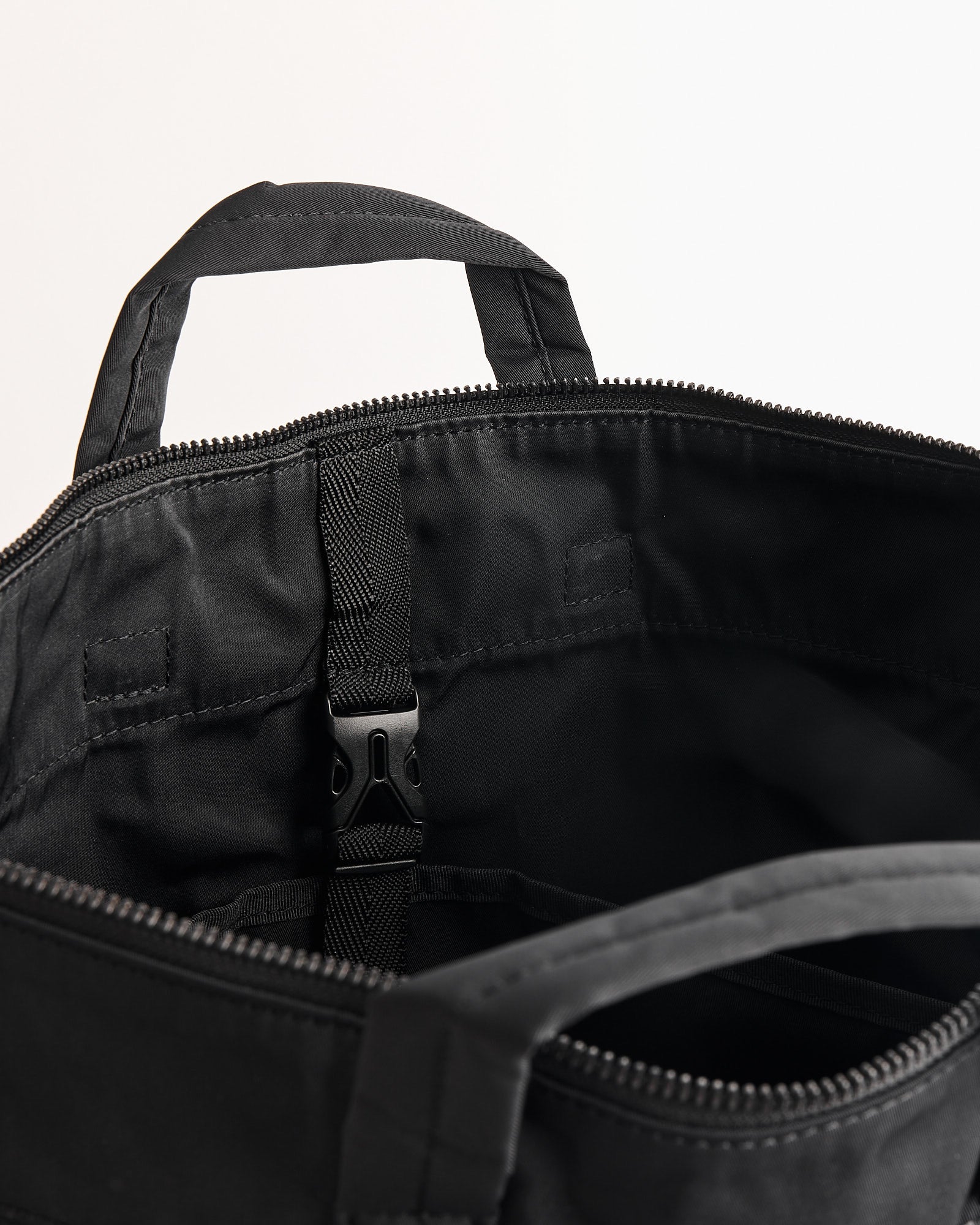 A close-up of the Amiacalva Gabardine Helmet Bag in Black shows its zip closure, two fabric handles, and interior black buckle fastener. Contact our online chat team for sizing or fit help. The bag is set against a plain white background.