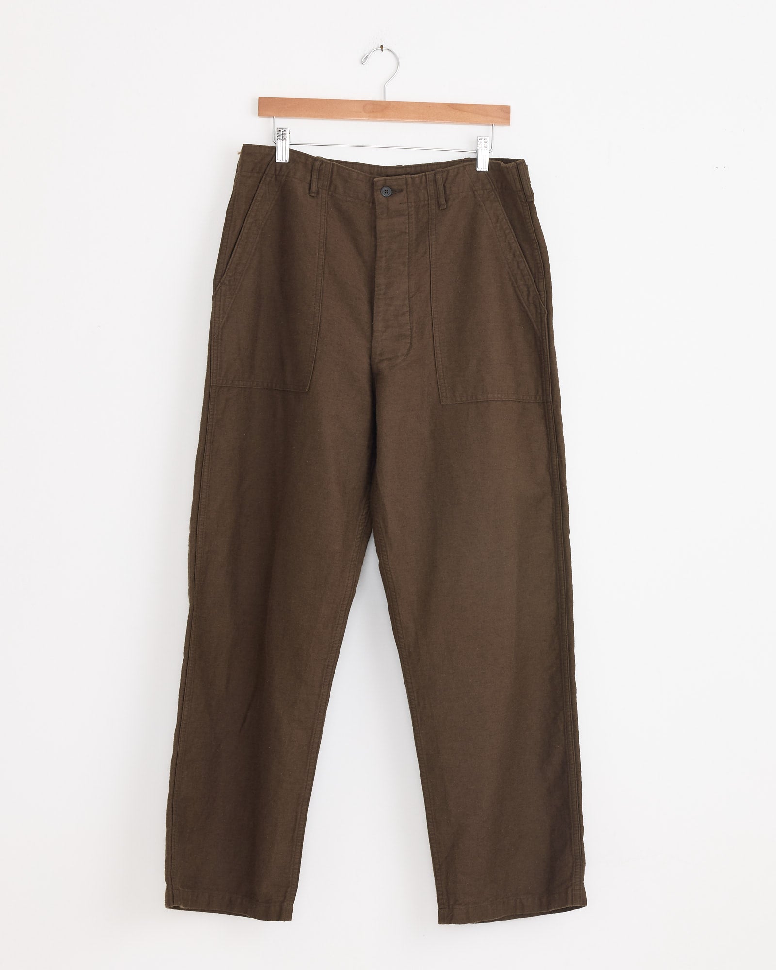 A pair of orSlow Relax Fit Fatigue Pant in Coffee Brown, crafted from cotton-linen moleskin with wide legs and front patch pockets, hangs on a wooden hanger against a white background.