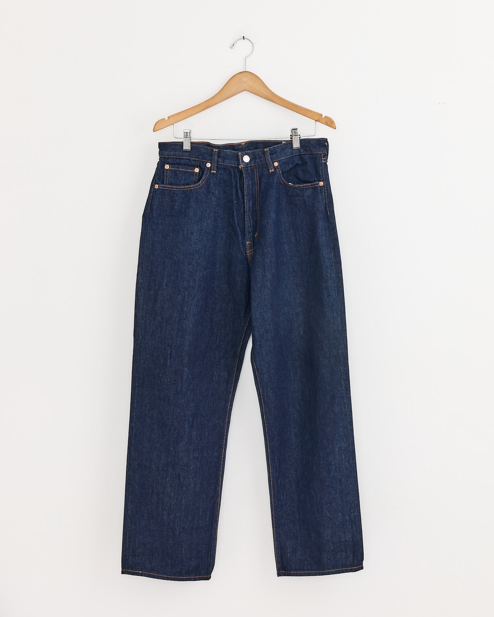 The orSlow 101 Dad's Fit Denim Pant in One Wash, featuring a straight-leg cut, hangs on a wooden hanger against a plain white wall.