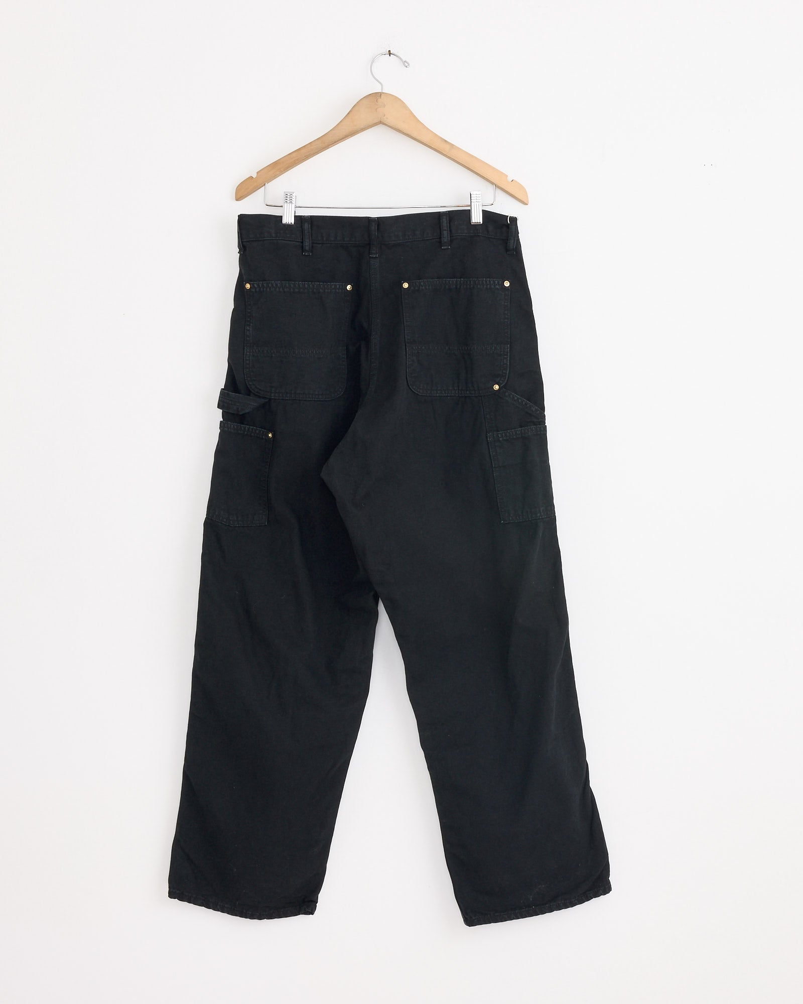 The orSlow Dad's Fit Oxford Painter Pant in Black, featuring multiple back and side pockets, hangs on a wooden hanger against a plain white wall.