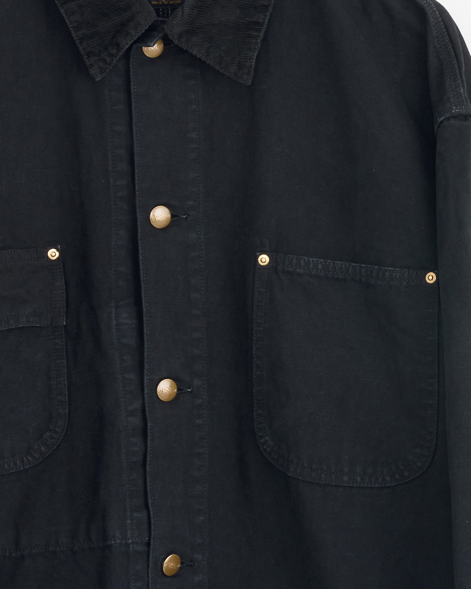 Close-up of the orSlow Relax Fit Oxford Coverall Jacket in Black, featuring gold buttons, two large front pockets, and a corduroy collar. Crafted from durable fabric, it combines classic style with workwear-inspired details.