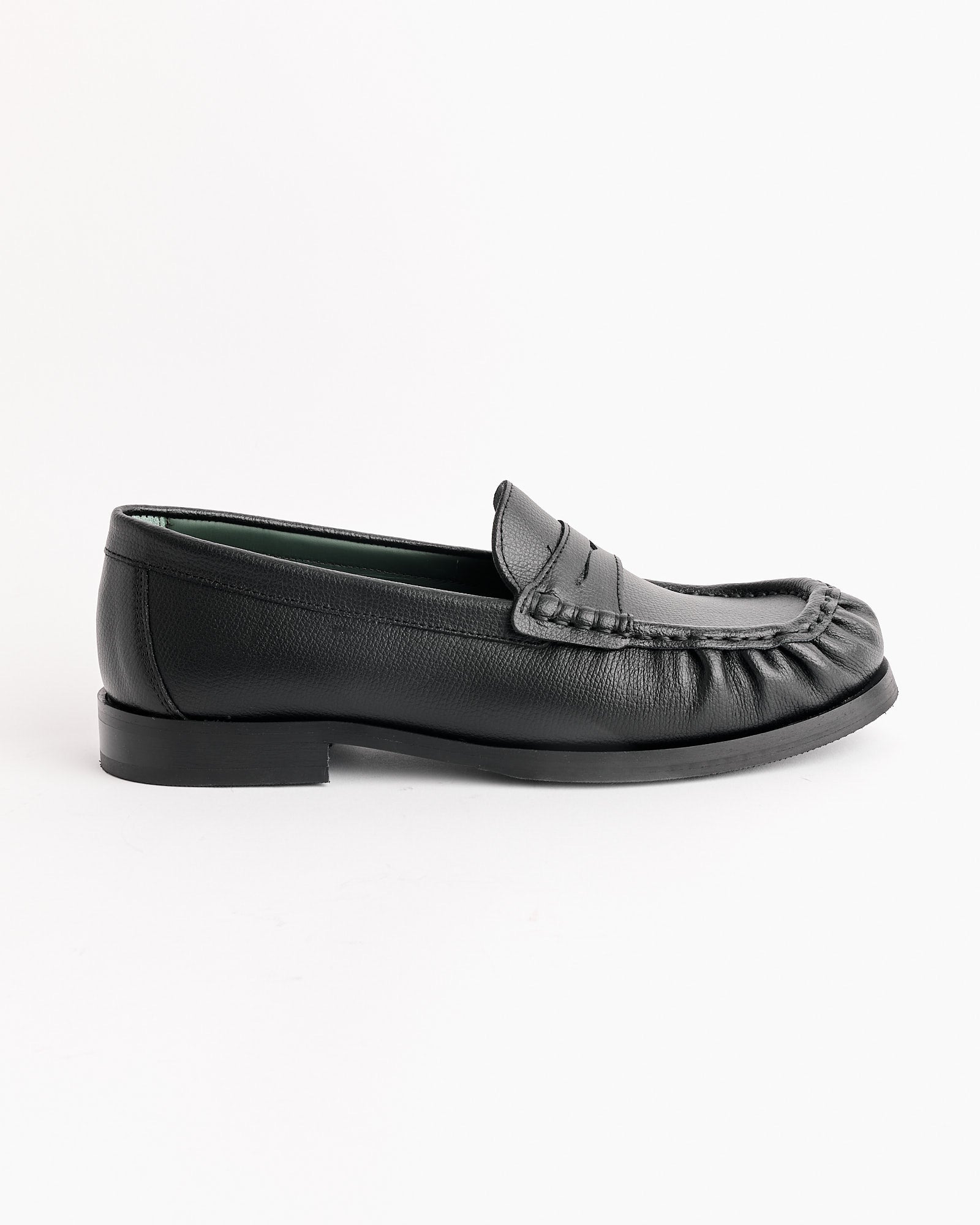 The Vinny's Ogee Loafer in Black features a low heel, moccasin-style stitching, ruffled toe box, and penny strap detail, shown on a white background.