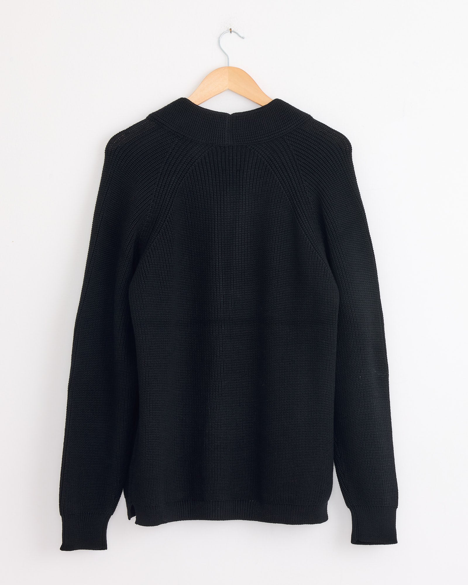 The Batoner Waso 1 Button Cardigan in Black, crafted in Japan from SOLIDWOOL yarn, is displayed from the back on a wooden hanger against a plain white wall.