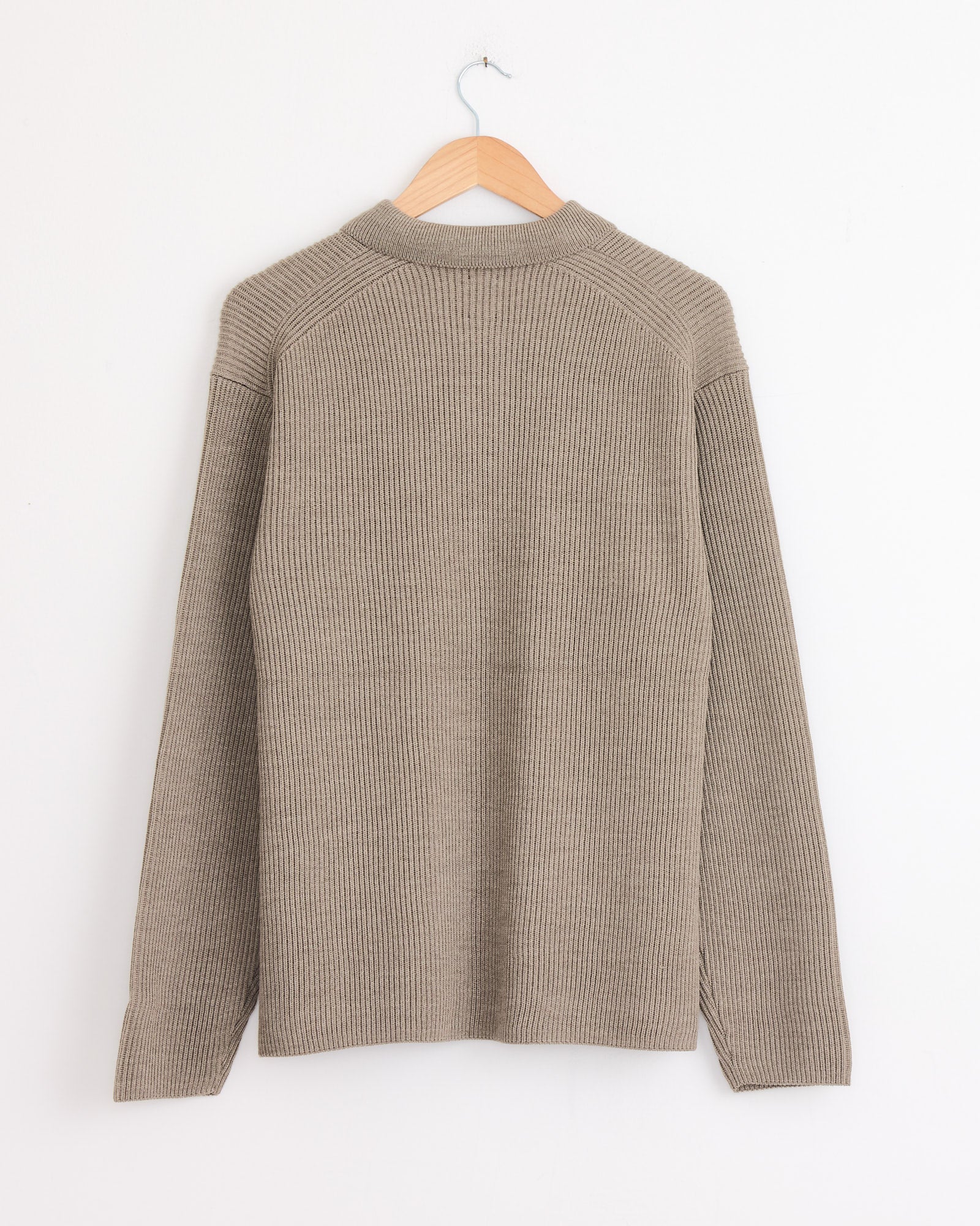 A Merange Brown, long-sleeve Batoner Zip Up Cardigan hangs on a wooden hanger against a white wall, shown from the back. Made in Japan, this wool sweater features a subtle ribbed texture for timeless style.