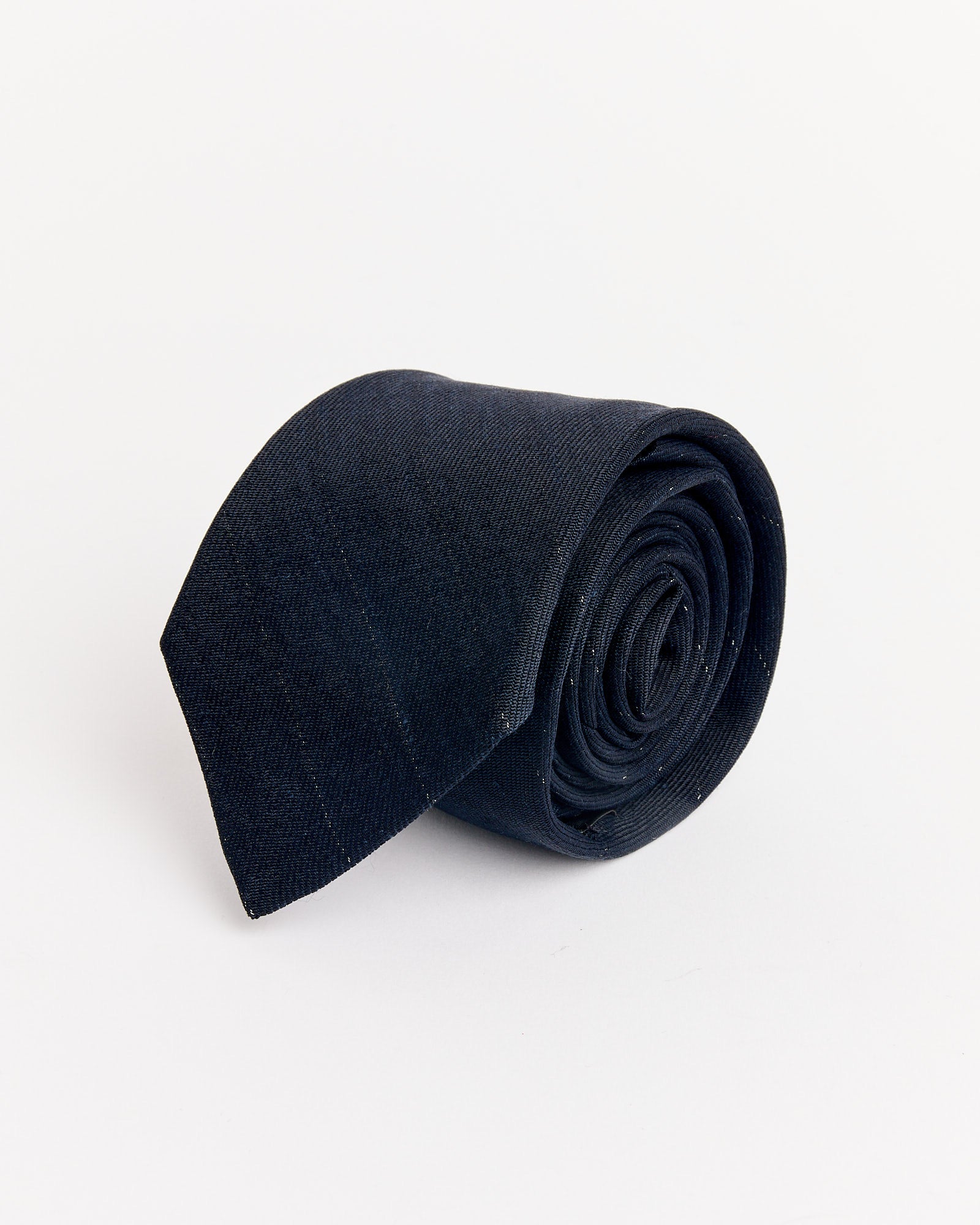 The Pinstripe Tie in Night by Our Legacy, a neatly rolled dark navy blue necktie, is displayed on a plain white background.