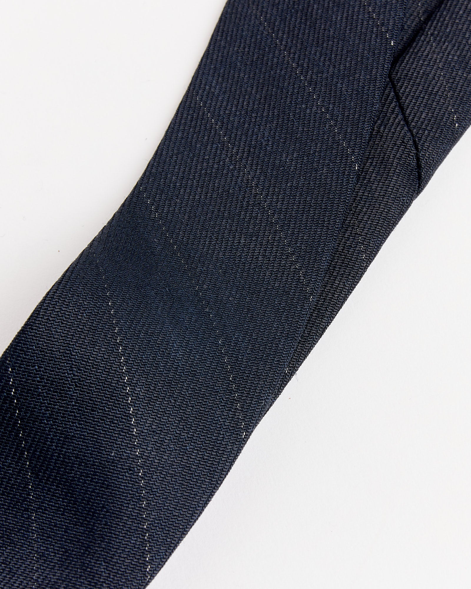 A close-up of the Our Legacy Pinstripe Tie in Night, featuring dark navy blue fabric with subtle diagonal stripes, displayed on a white surface.