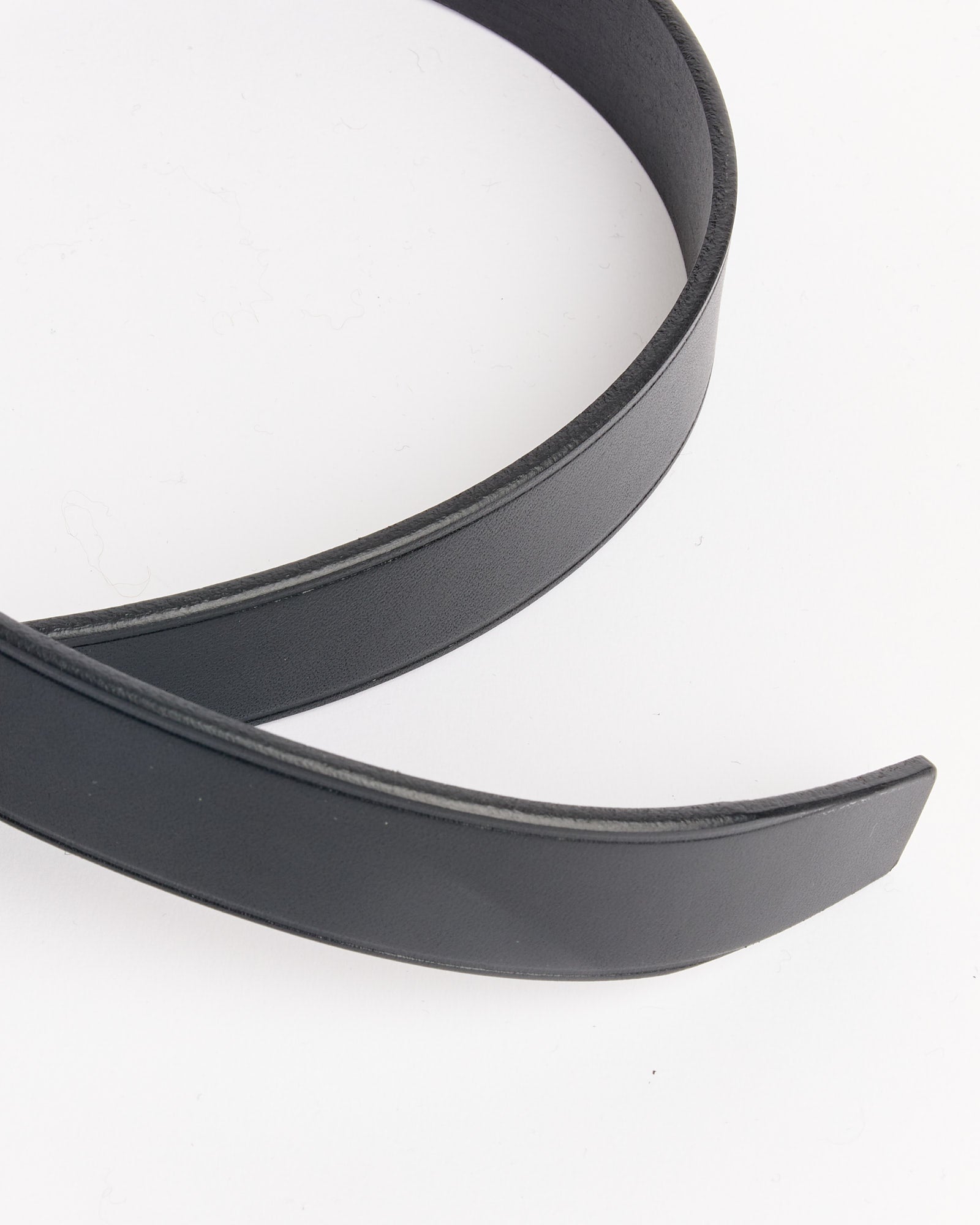 A close-up of the Comme Des Garçons Homme 301 Belt in Black, featuring a pointed tip and elegant curve, shown partially on a white surface.