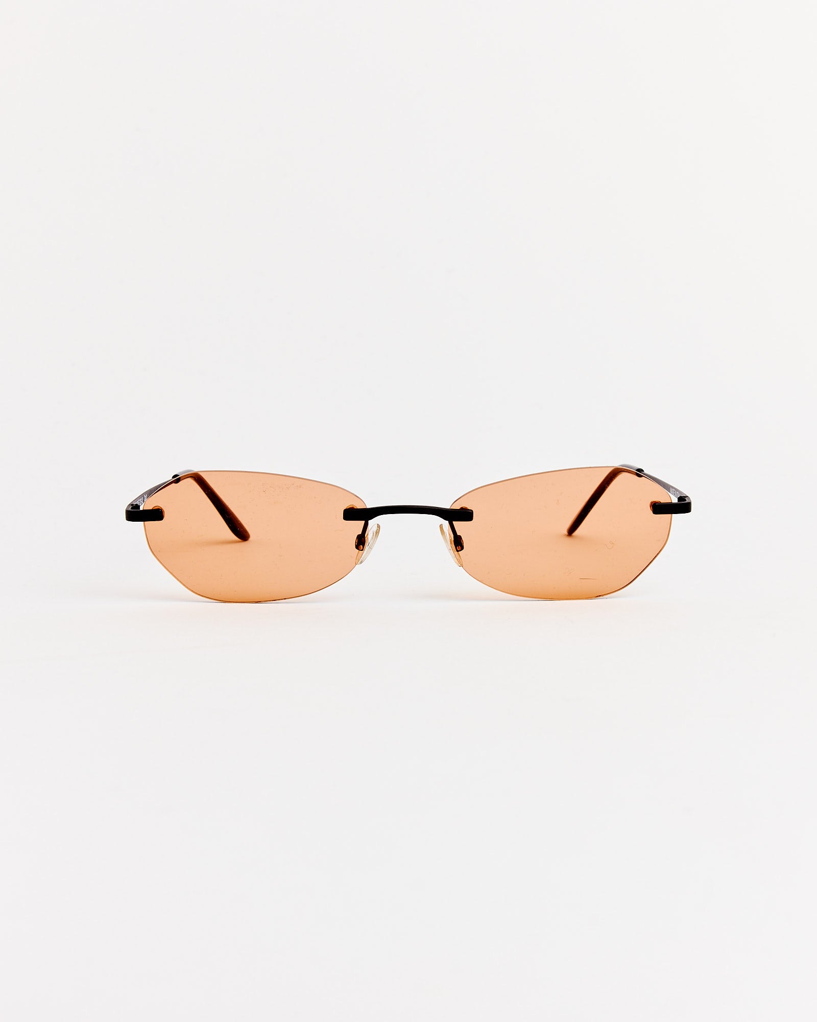 The Adorable Sunglasses in Graphite Spectra by Our Legacy feature rimless light orange-tinted lenses and thin black temples, shown on a plain white background.