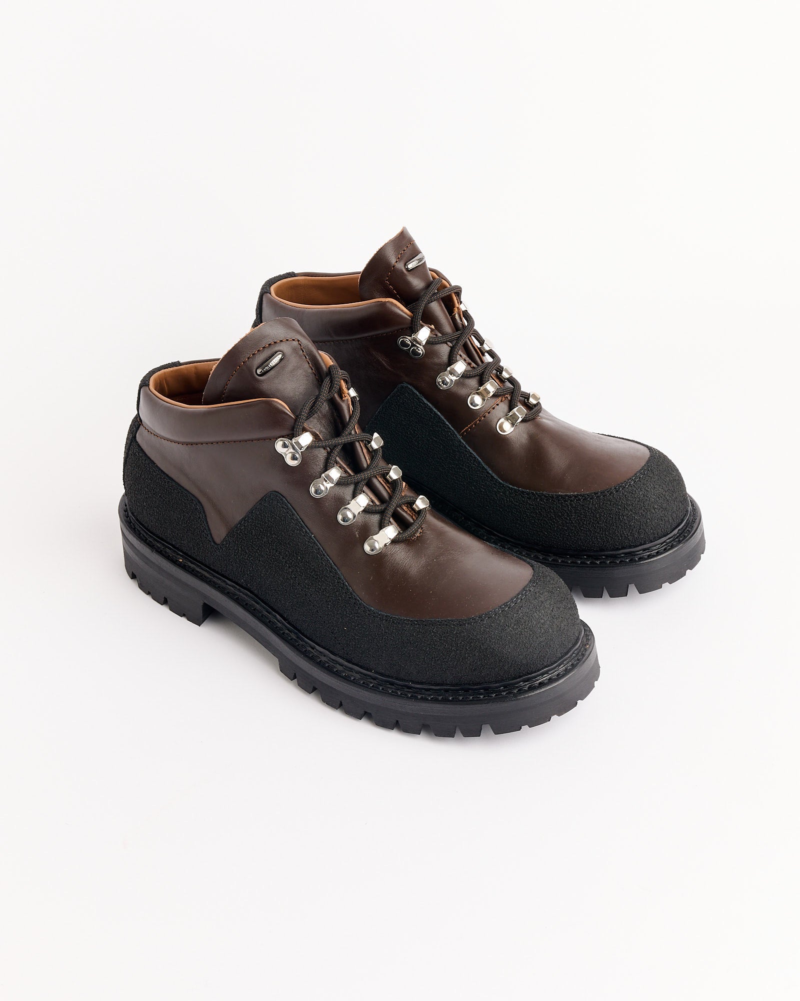 Our Legacy Quest Boot in Maduro Brown features dark brown leather, black textured toe caps and soles, silver eyelets, black laces, and tan interiors, shown on a white background.