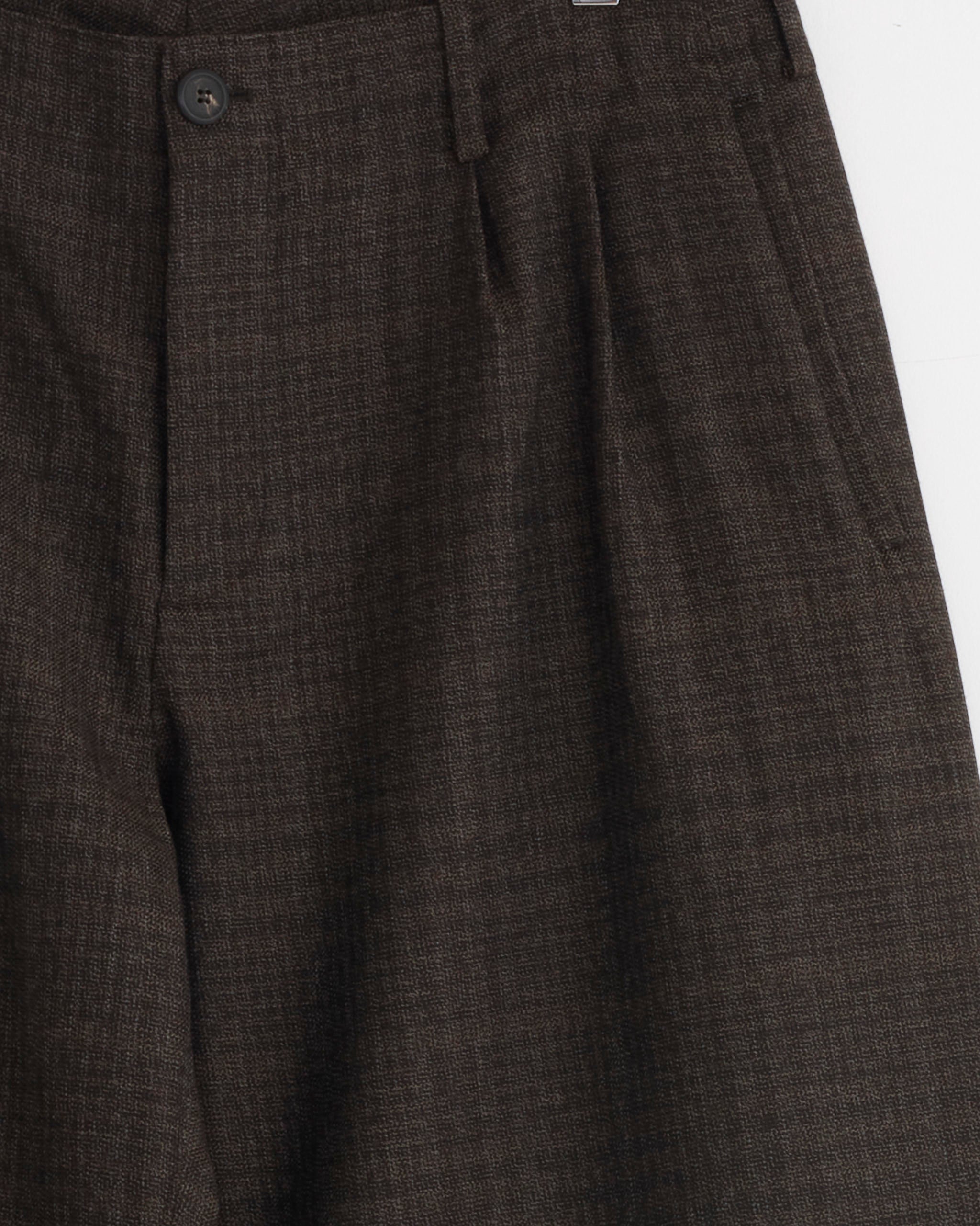 Close-up of Our Legacy's Bridge Chino in Brown, crafted from textured Italian virgin wool with pleats, side pockets, a black button, and wide-leg fit, shown against a white background.