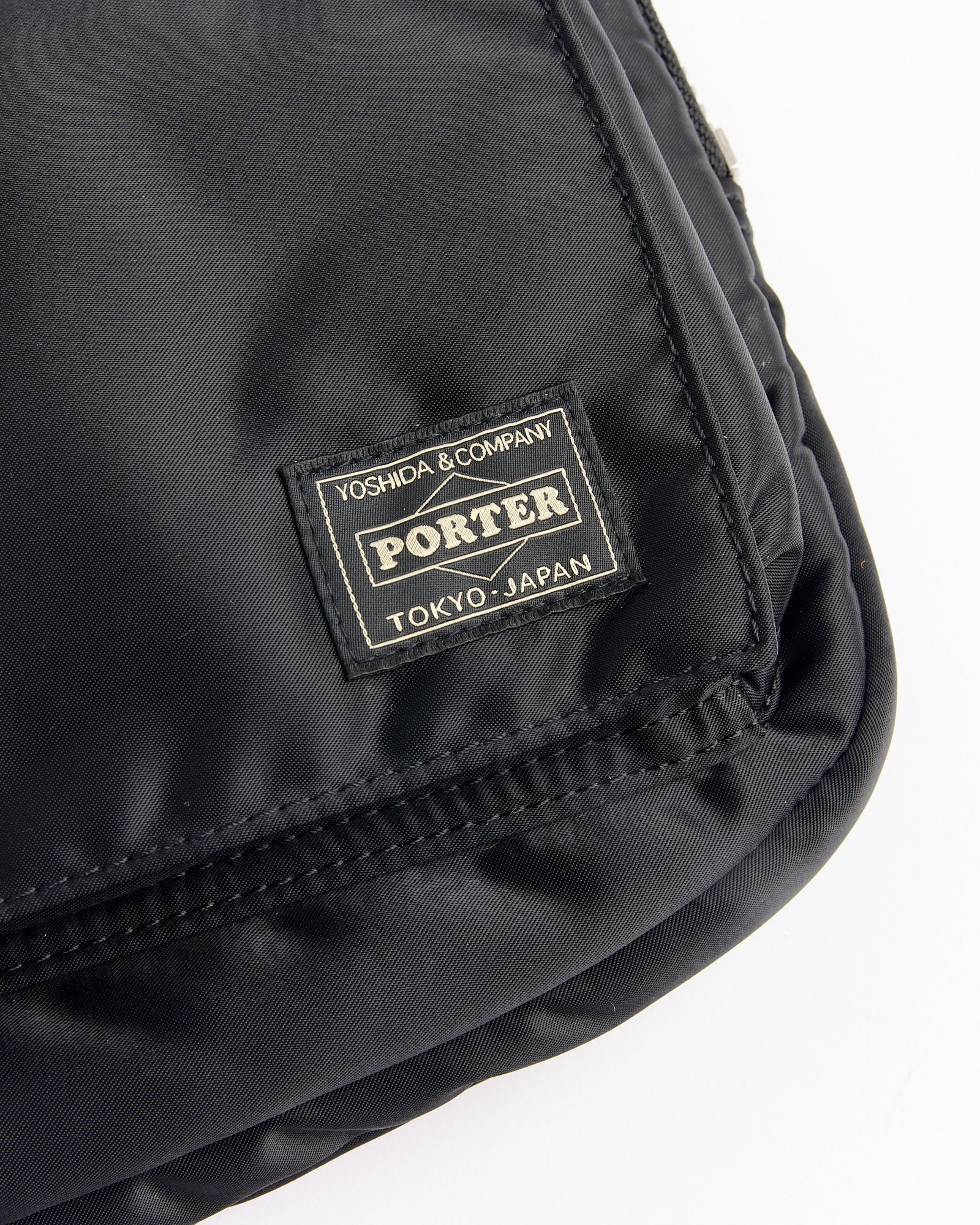 Close-up of the Porter Tanker Document Case in Black, featuring smooth, shiny nylon fabric and stitched edges, with a label that reads "Yoshida & Company Porter Tokyo, Japan" in white text.