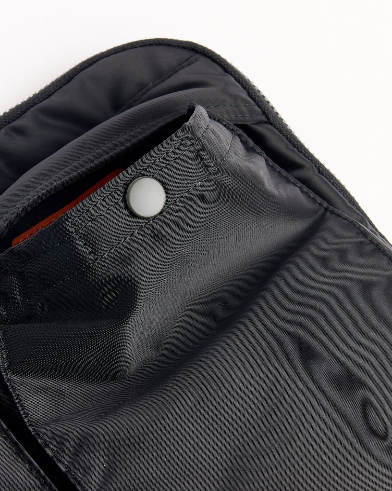 Close-up of the Porter Tanker Document Case in black, featuring visible stitching, a round matte snap-button flap, and a glimpse of the orange interior lining.