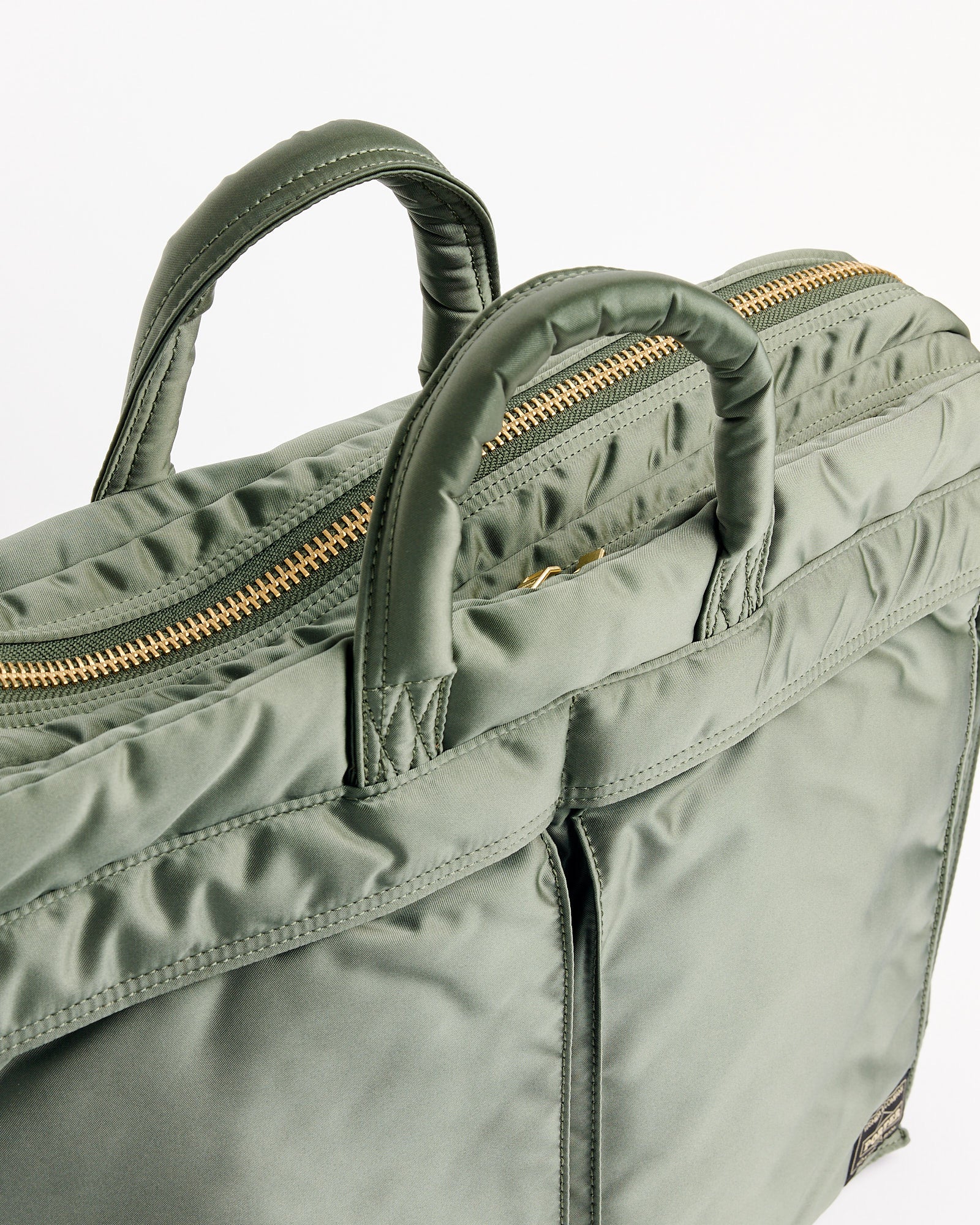 A close-up of the Porter Tanker 2Way Document Zip Bag in sage green nylon, featuring padded handles, a gold zipper, sleek smooth texture, and edge stitching detail.