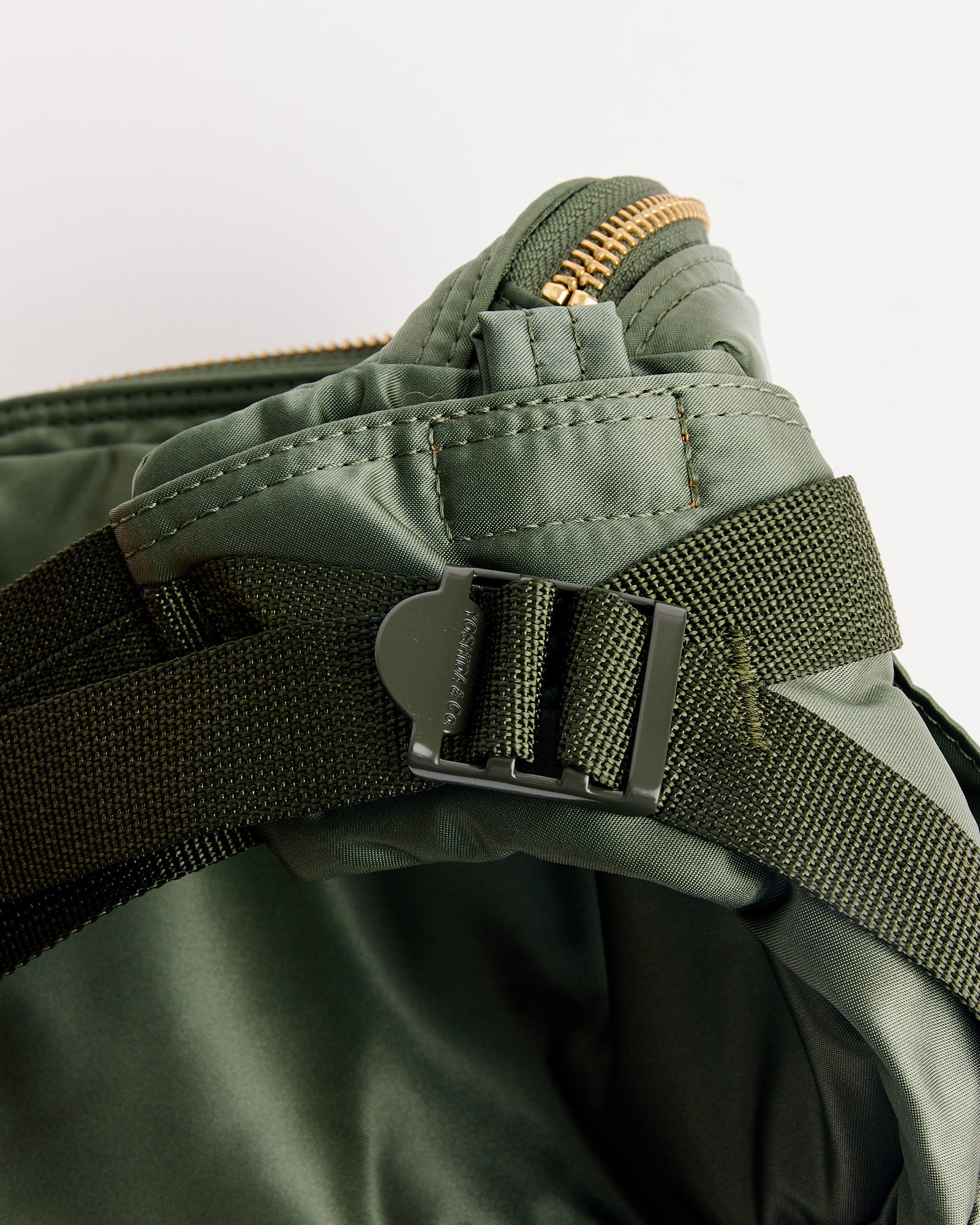 A close-up of the Porter Tanker Fanny Pack in Sage Green, highlighting its black plastic buckle, black strap, gold zipper, and detailed stitching against a white background.