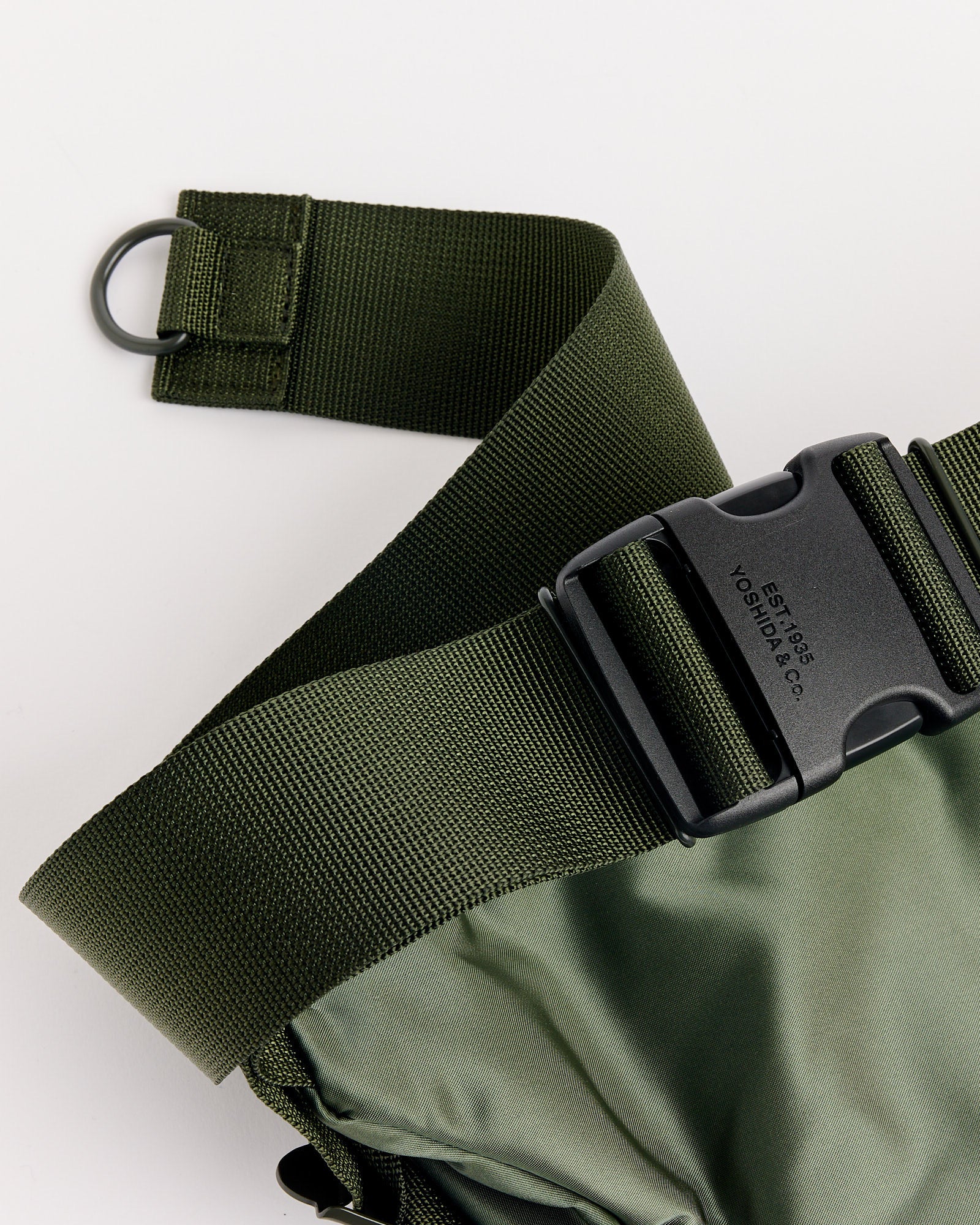Close-up of the adjustable olive green strap with black plastic buckle and D-ring on the Porter Tanker Fanny Pack in Sage Green, attached to its shiny green fabric.