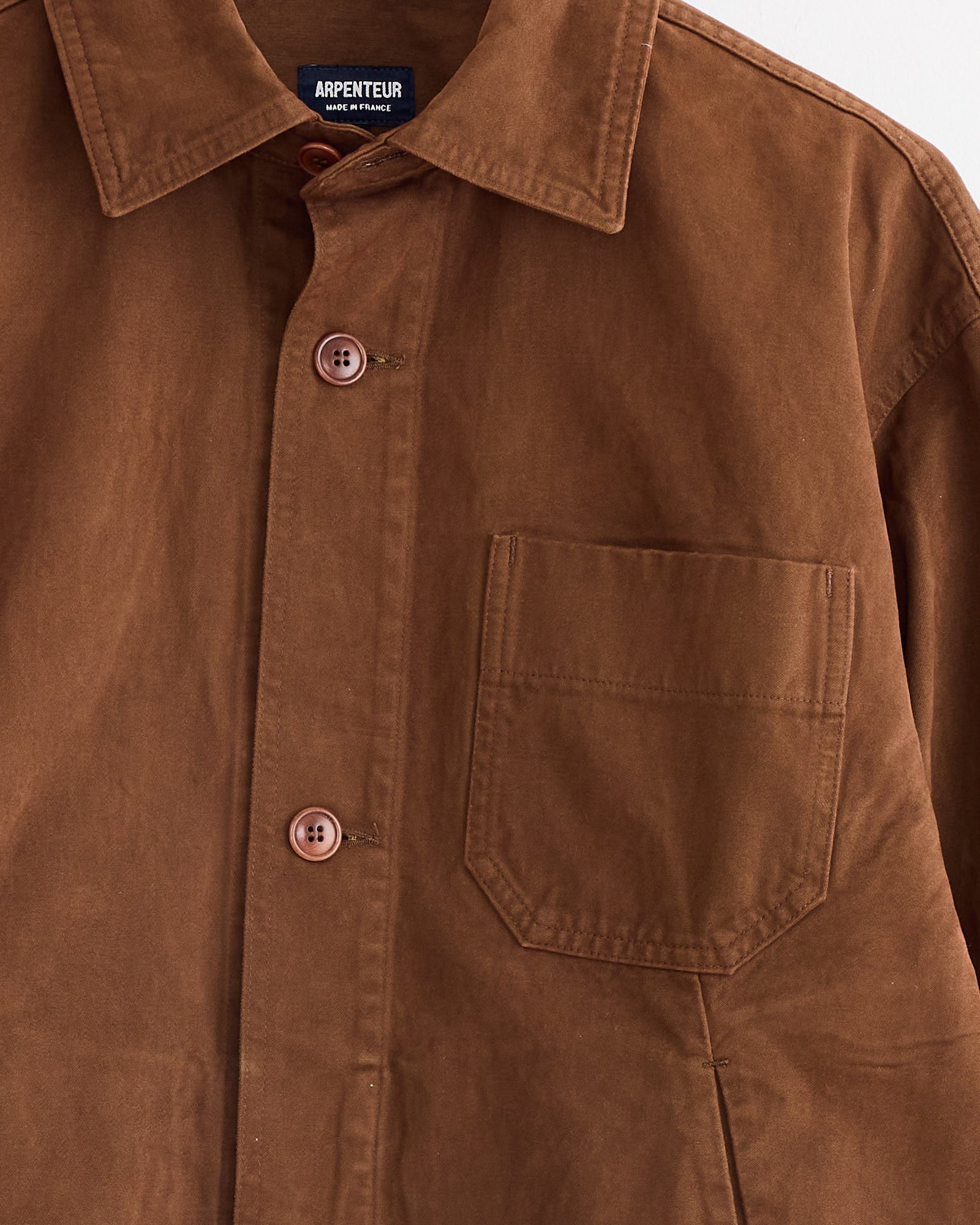 The Arpenteur Lux J Unlined Jacket in Tobacco features a button-up front, collared design, left chest pocket, visible stitching, brown buttons, and an Arpenteur label inside the collar, inspired by classic workwear styles.