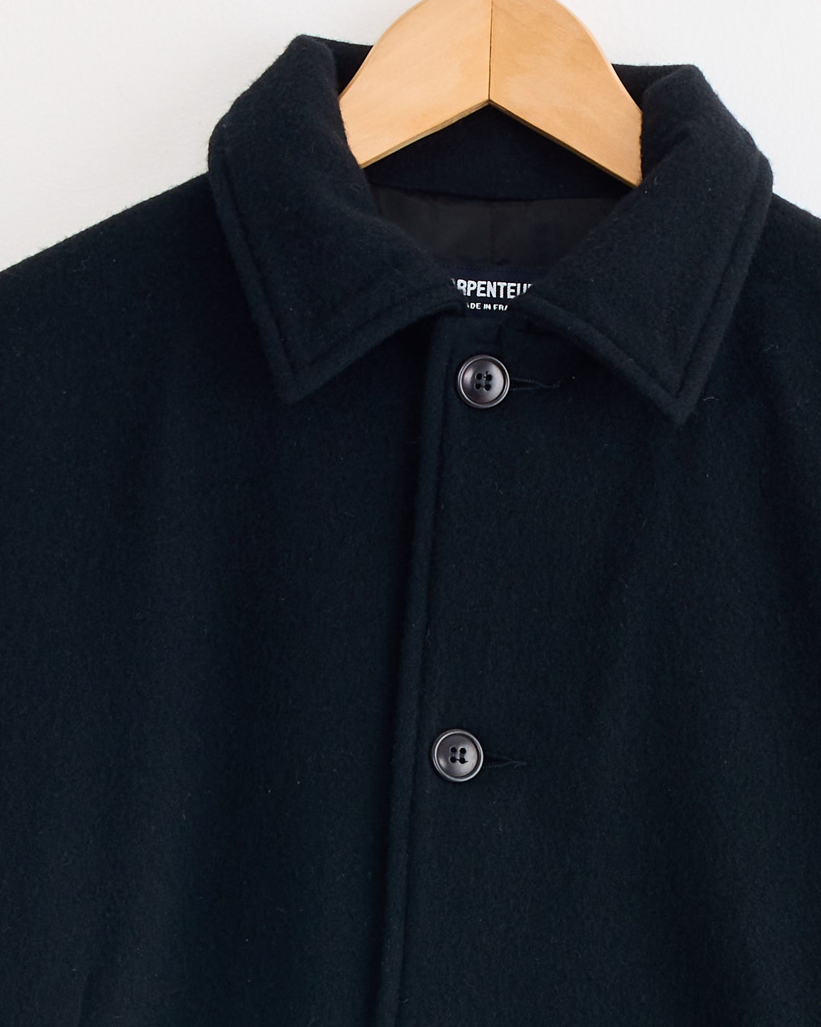 A close-up of the Arpenteur Lux J Lined Jacket in Black on a wooden hanger, highlighting its collar, two buttons, and a partially visible inner label.