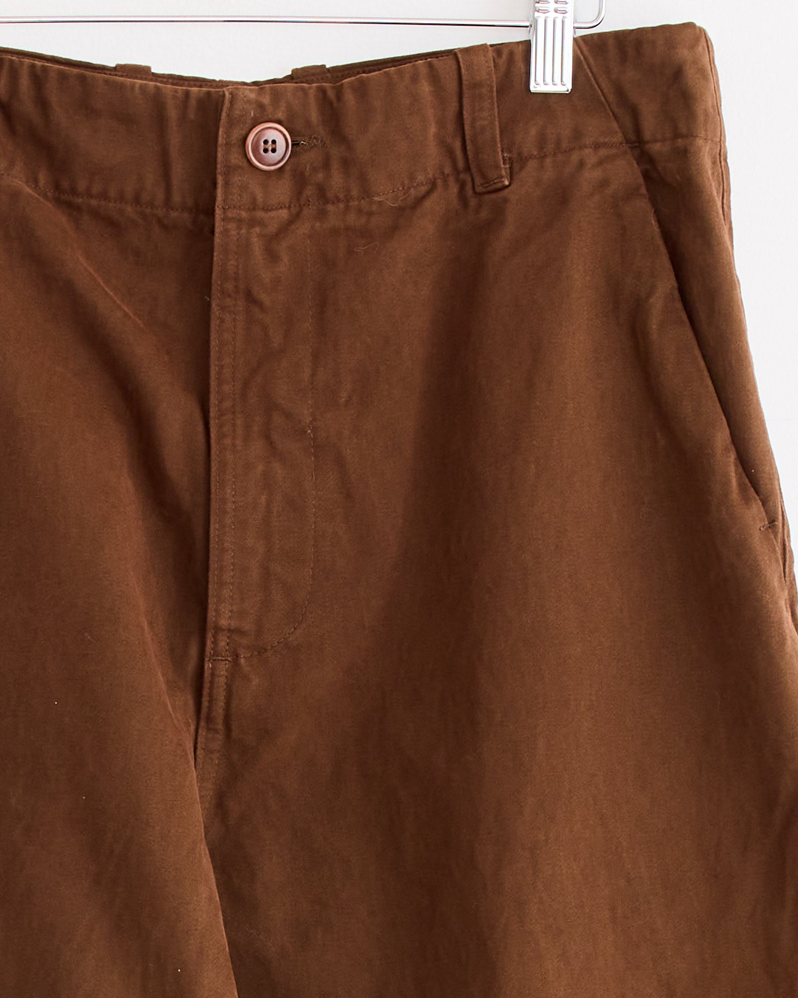 Close-up of Arpenteur's Lux P Trouser in Tobacco, made in France, displayed on a hanger and featuring a button closure, belt loops, and pockets.
