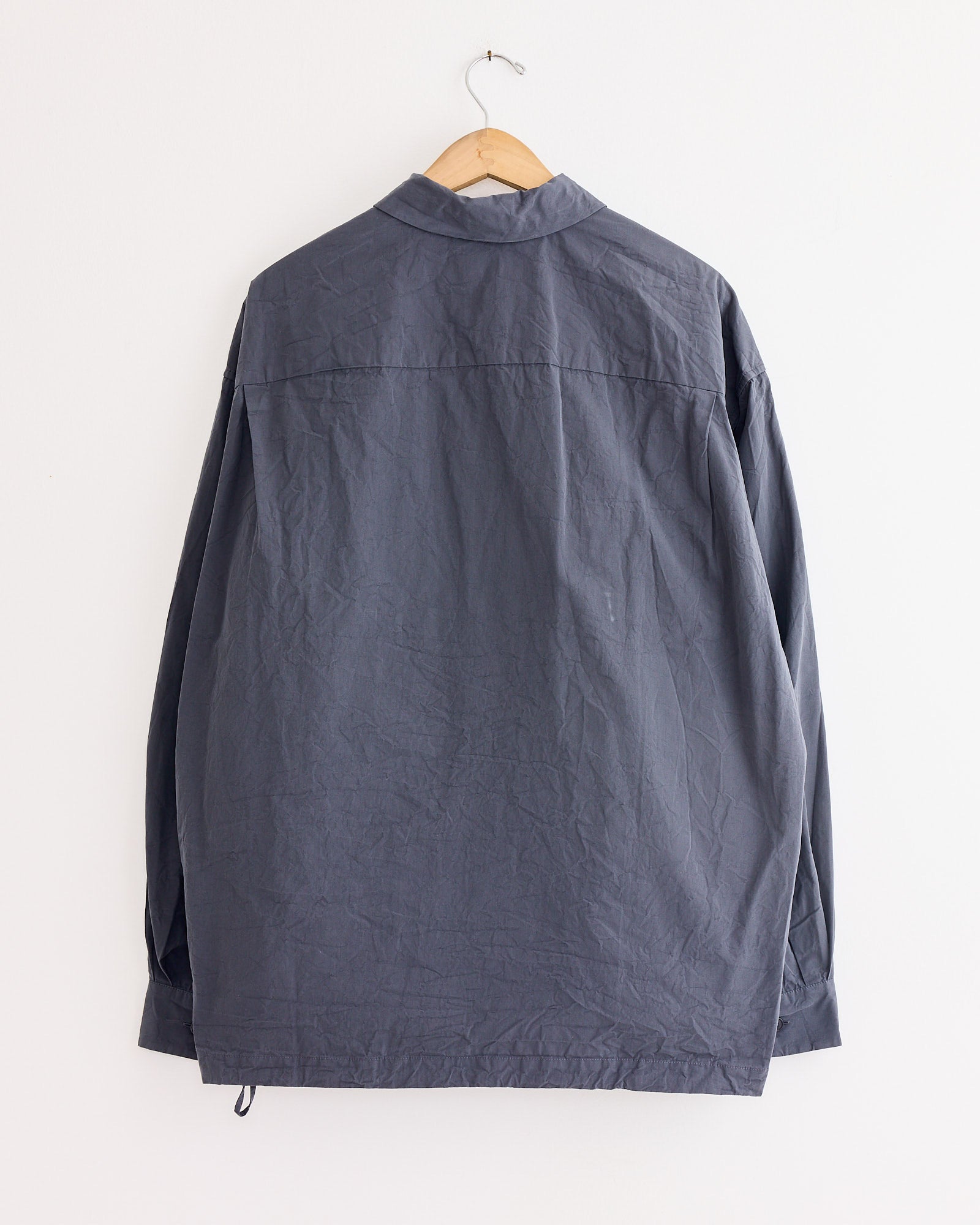 A long-sleeved Casey Casey Mika Shirt in Blu Skull with a collar hangs on a wooden hanger against a white wall, shown slightly wrinkled and from the back.