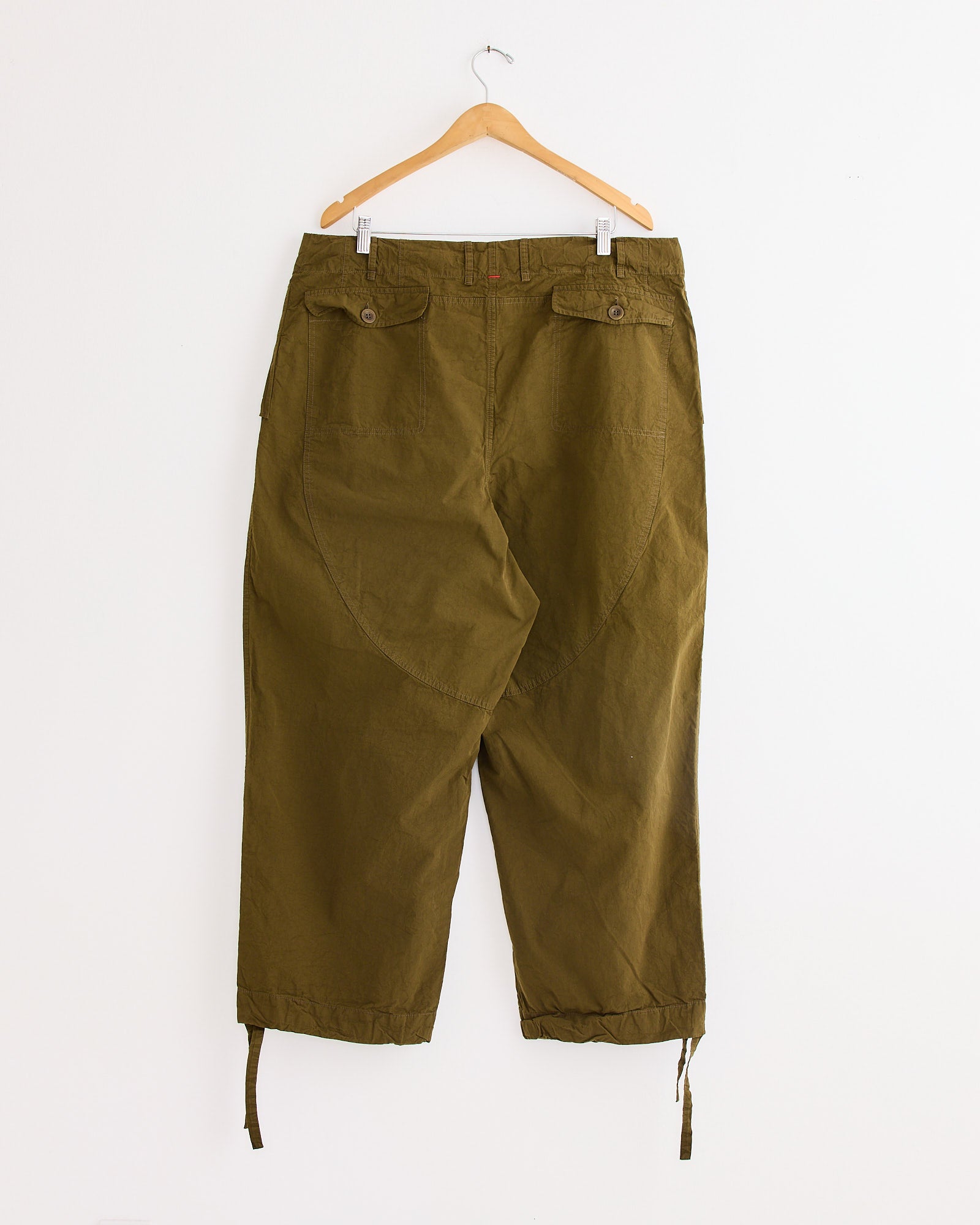 The Casey Casey Abel Pant in Green Lake, made from paper cotton, hangs on a wooden hanger against a white background. This relaxed drawstring pant features button-flap back pockets and adjustable drawstring hems.