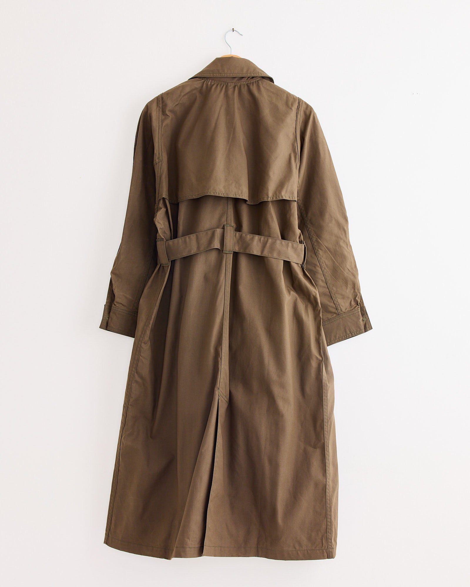 The Jesse Kamm Car Coat in Loam hangs on a hook against a plain white wall, shown from the back with a belted waist and a relaxed fit.