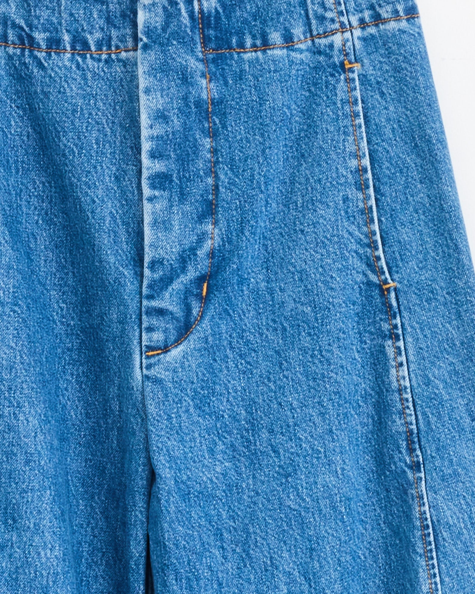 Close-up of the Shaina Mote Lune Pant in Medium Blue, crafted from premium Italian denim with orange stitching, side pocket, detailed seams, waistband accents, and a subtle balloon leg silhouette.