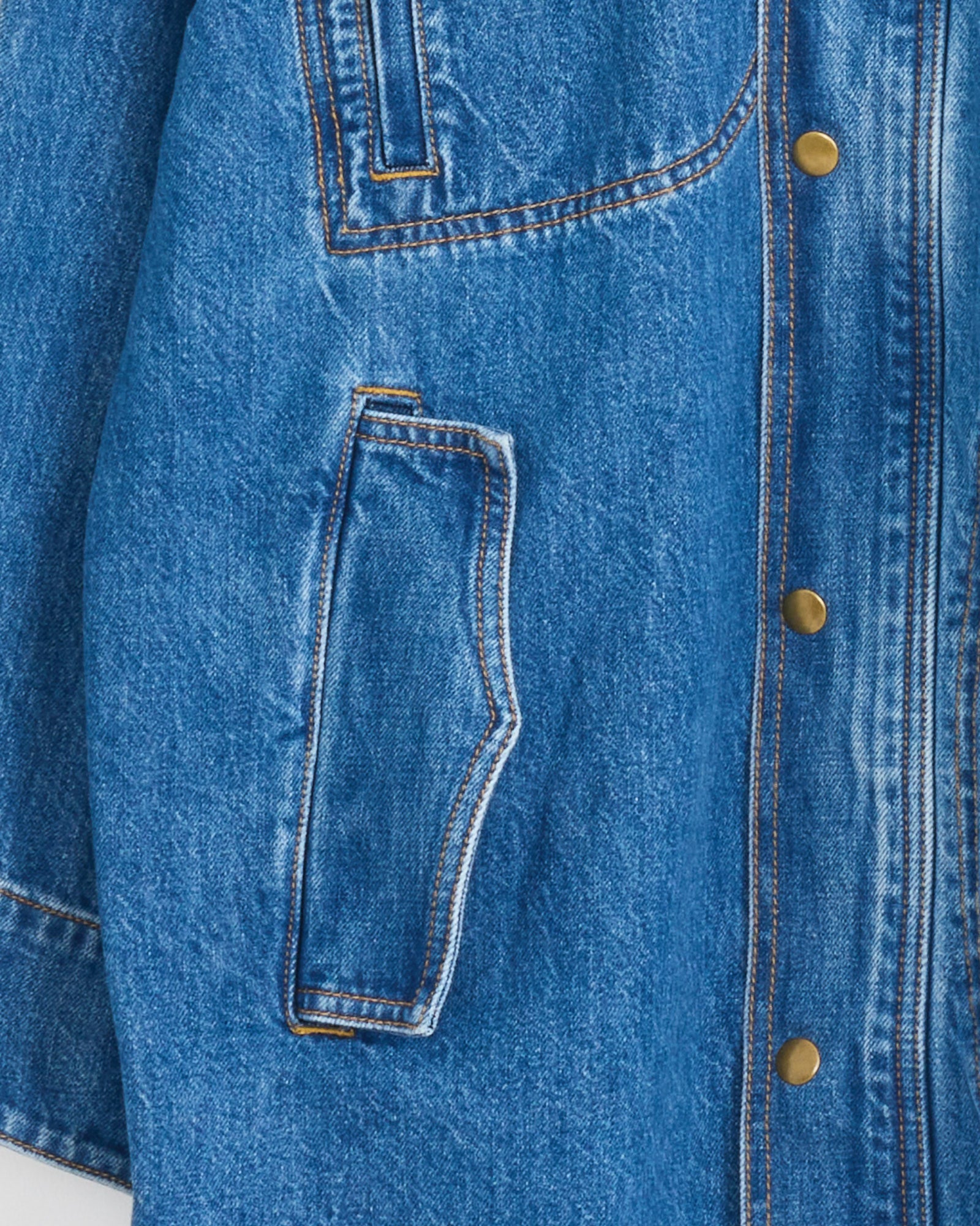 Close-up of Shaina Mote's Town And Country Coat in Medium Blue, featuring contrast stitching, brass snap buttons, and an angled front pocket—a refined update on the classic utility jacket.