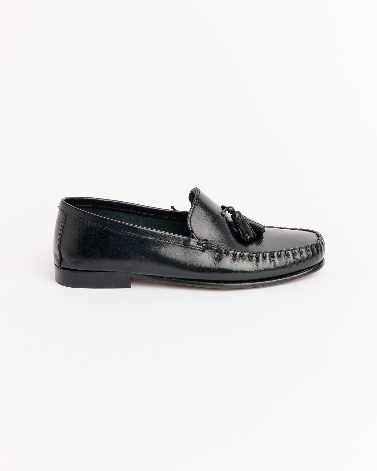 The Jamie Haller Tasselo Moc Loafer in Black features tassels and moccasin-style stitching, shown in profile on a white background. Unsure about sizing? Use our online chat to find your perfect fit.