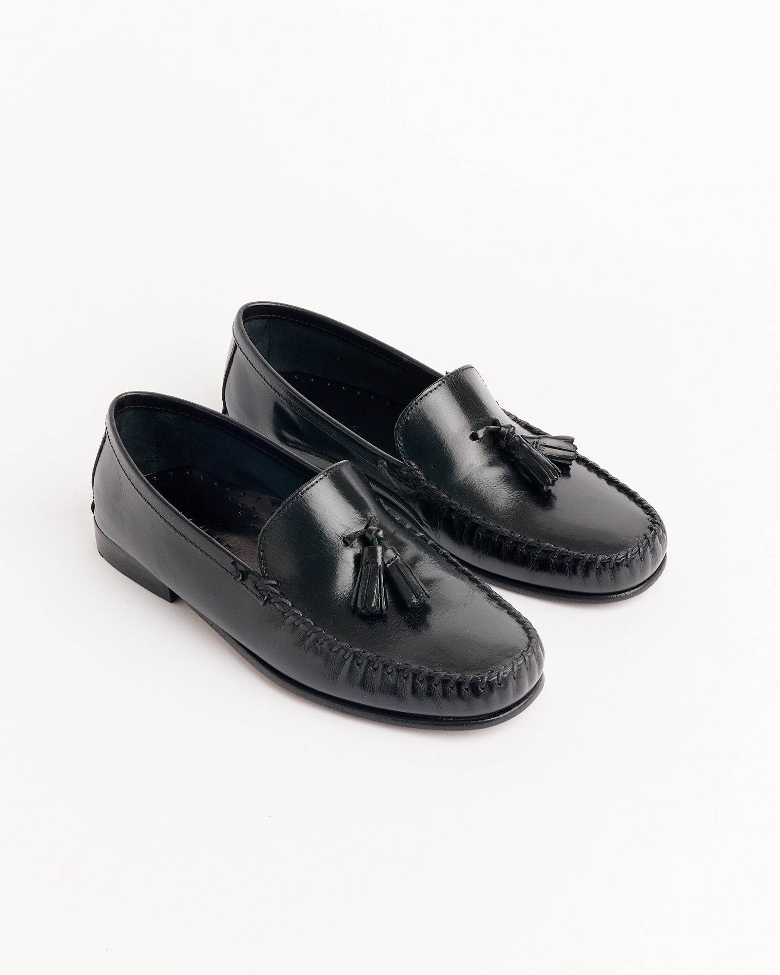 The Tasselo Moc Loafer in Black by Jamie Haller features tassels and moccasin-style stitching, shown on a white background. For sizing or fit questions, use our online chat to find your perfect pair.