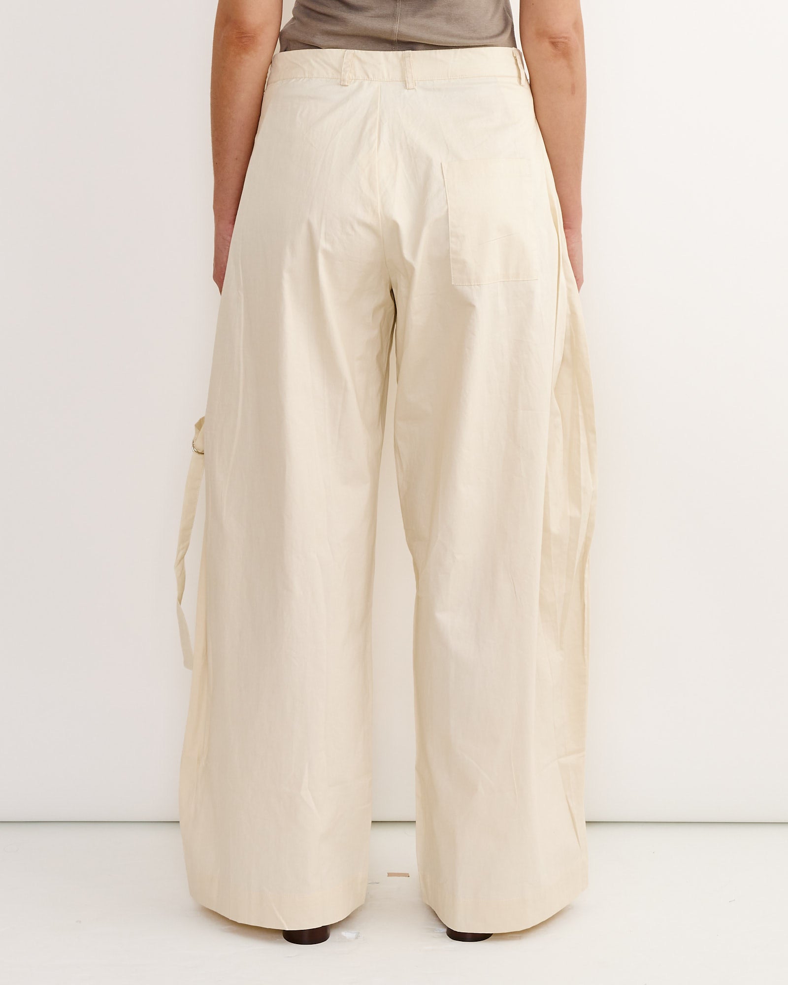 Back view of a person wearing Deiji Studios Tab Pant in Off White, a loose-fit, wide-leg trouser with a back pocket and side belt detail, standing against a plain white background.
