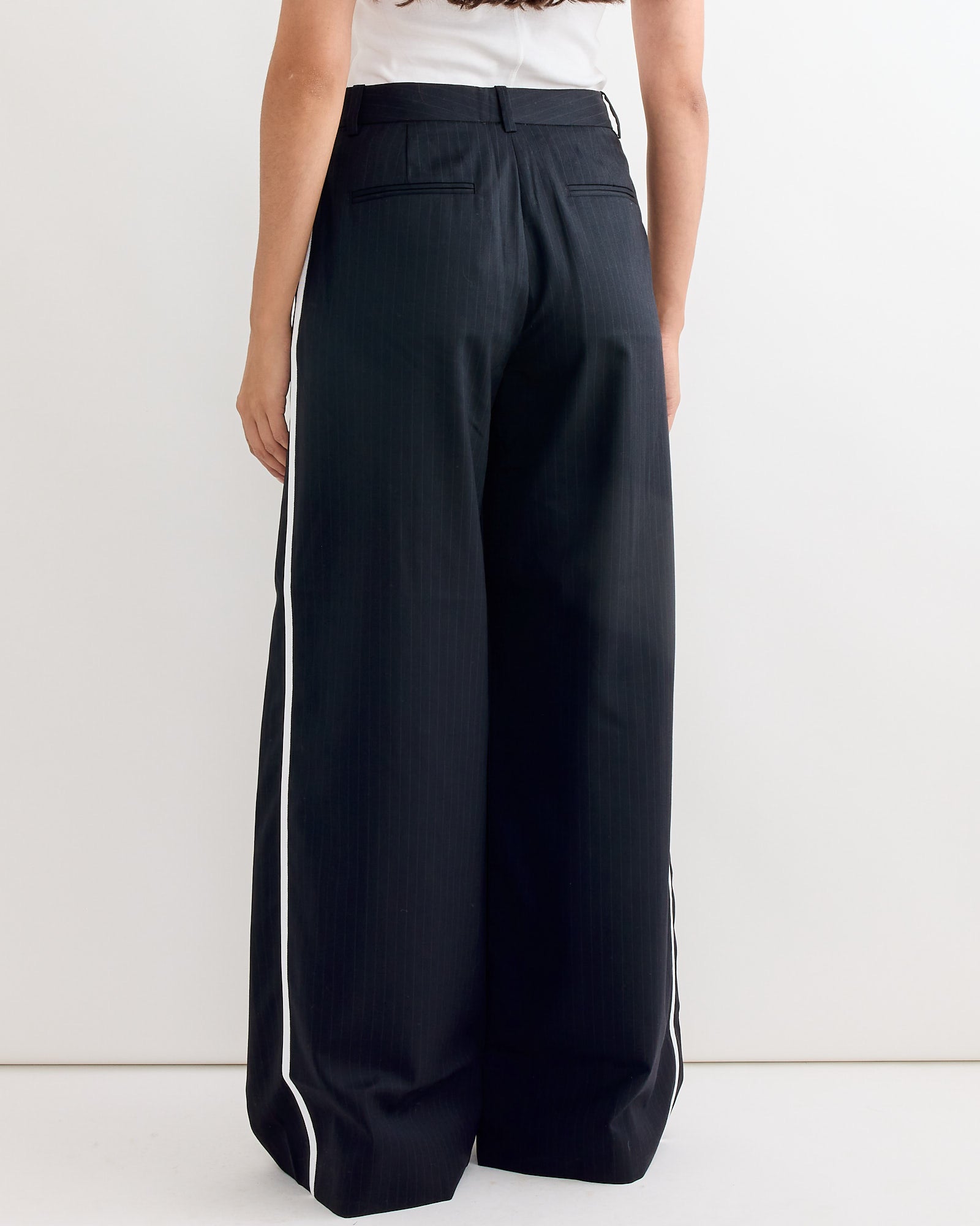 A person is shown from the back in ST. AGNI’s Side Stripe Homme Pant in Black Pinstripe and a white top—ideal for online chats about outfit sizing or fit inspiration.