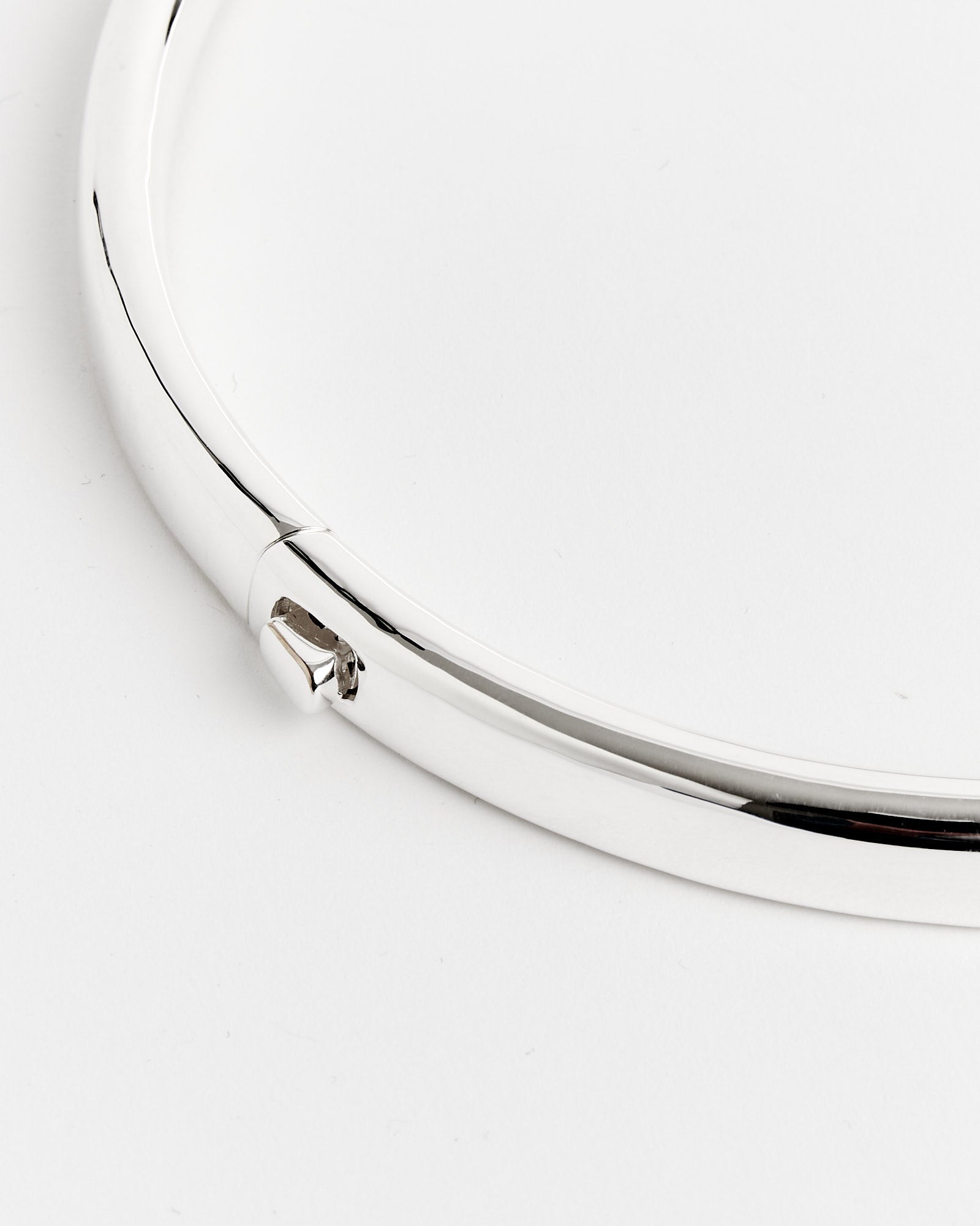 A close-up of the Completedworks Recycled Brass Neck Collar, featuring its smooth, circular design and clasp, set against a white background—ideal for those seeking sizing advice via online chat.