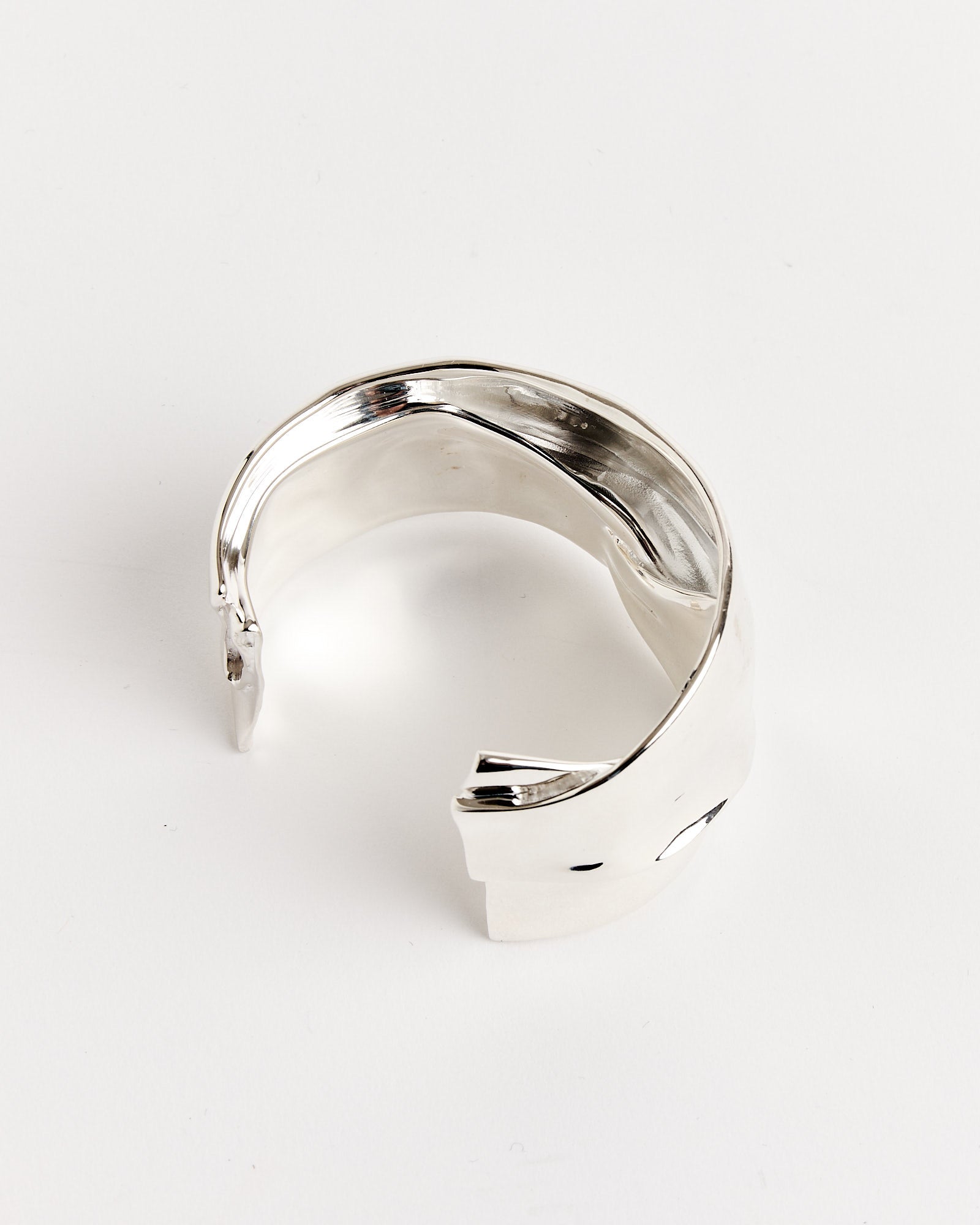 The Small Brass Cuff by Completedworks is a modern, open-ended bracelet with a smooth, slightly twisted design. For sizing or fit questions, please use our online chat. Shown against a plain white background.
