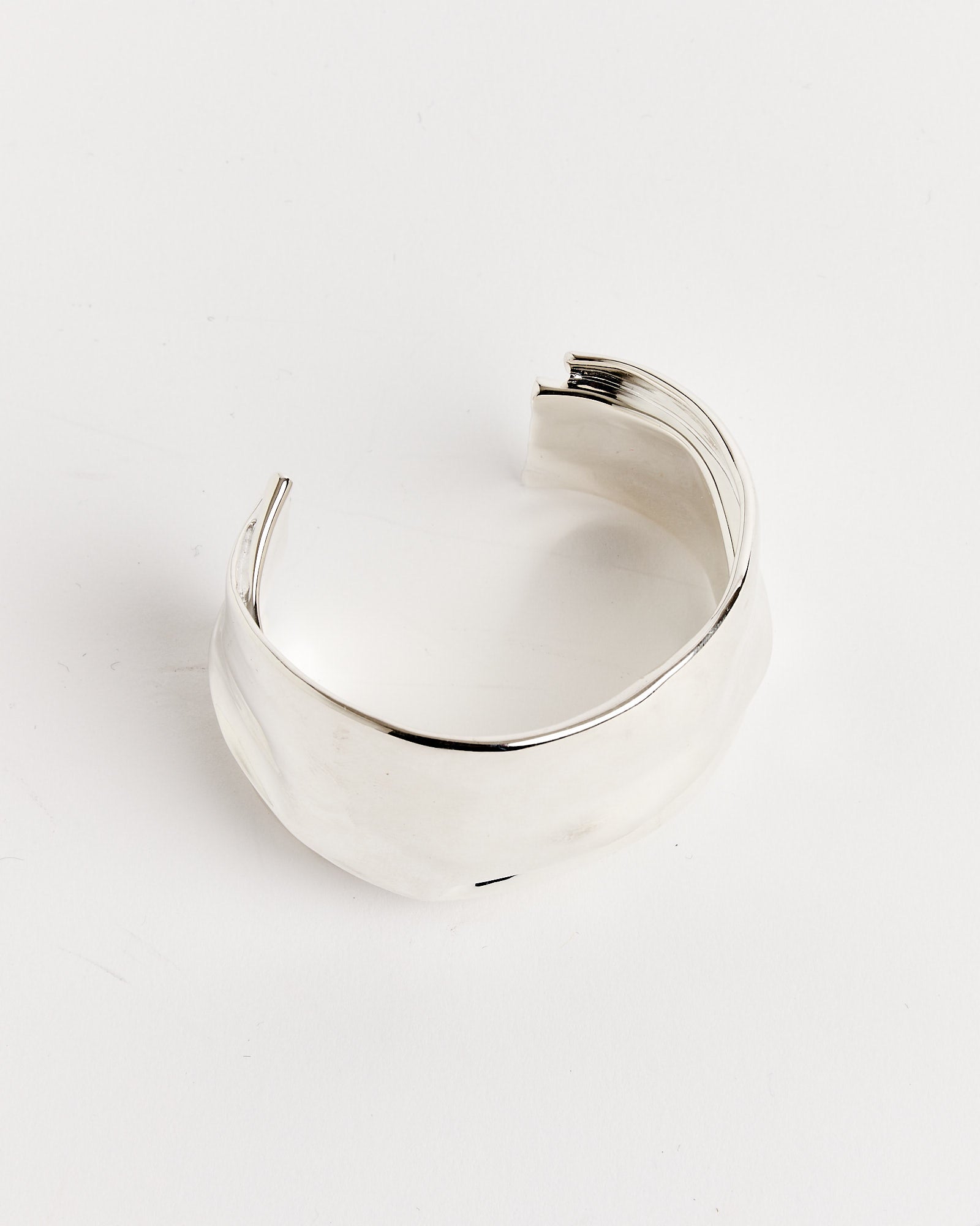 The Small Brass Cuff by Completedworks features a wide, slightly irregular wavy design and is shown on a white background. Contact us via online chat for sizing and fit questions.