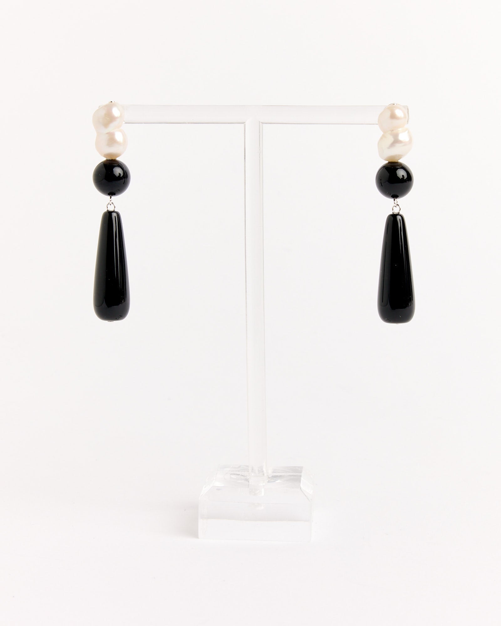 The Completedworks Recycled Silver Black Onyx FWP Earrings feature irregular white pearls, round black beads, and long glossy black teardrop pendants. Displayed on a clear stand. For sizing details, use our online chat.