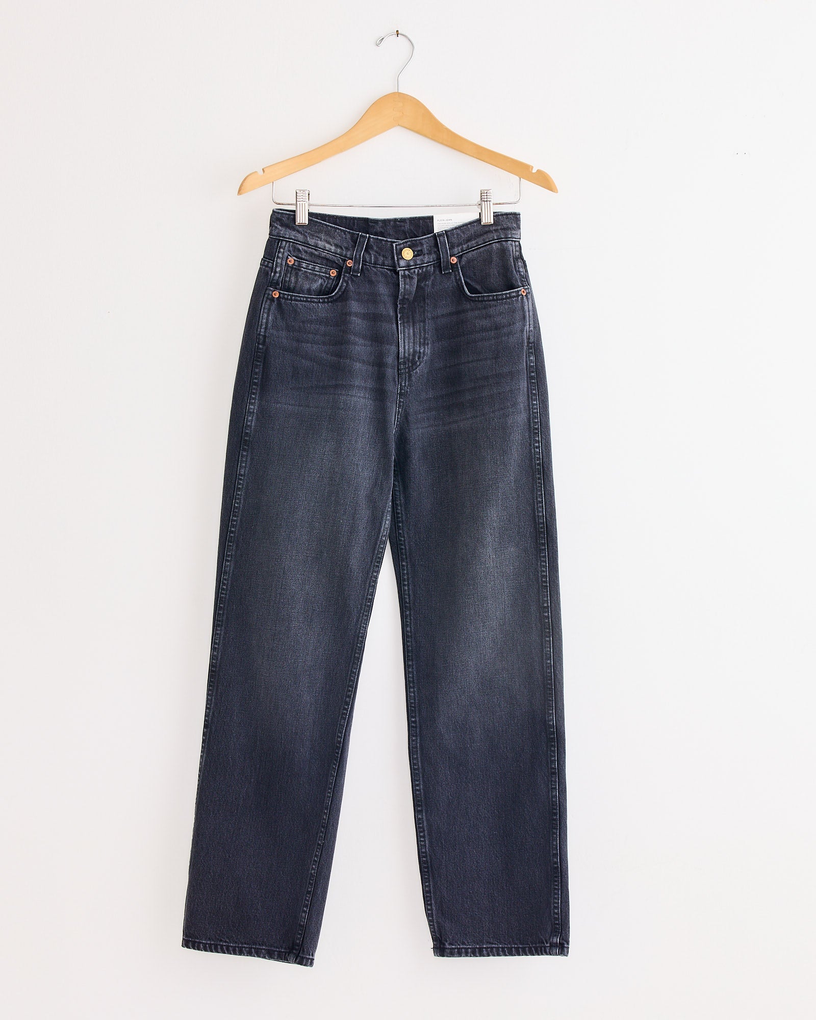 The Plein Jean in Stil Black by B Sides, a pair of high-rise, straight-leg denim jeans, is displayed on a wooden hanger against a plain white wall.