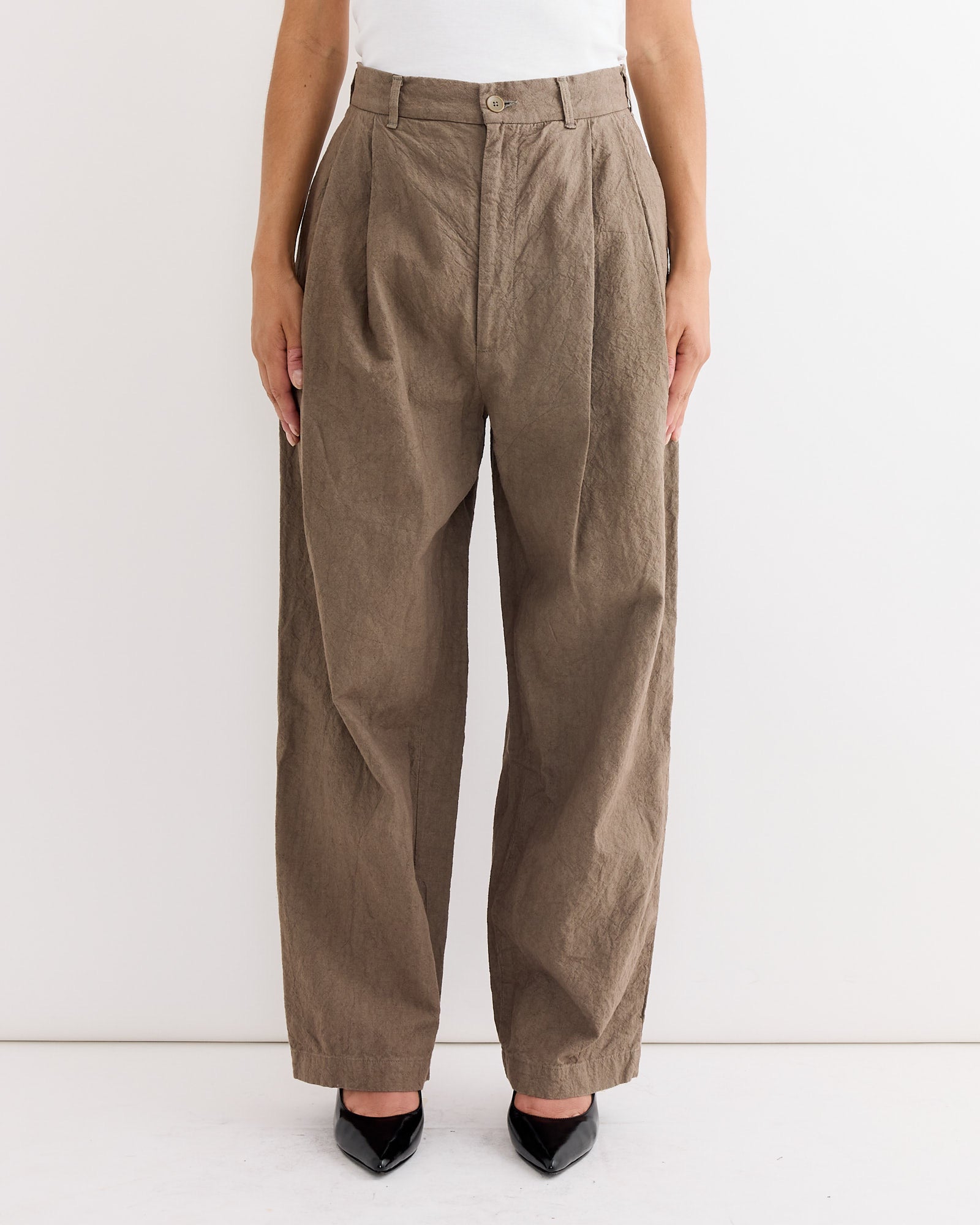 A person models the Black Crane Crinkled Trouser in Khaki, featuring a high waist and loose fit, paired with black pointed-toe shoes. Only the lower torso and legs appear against a plain white background.