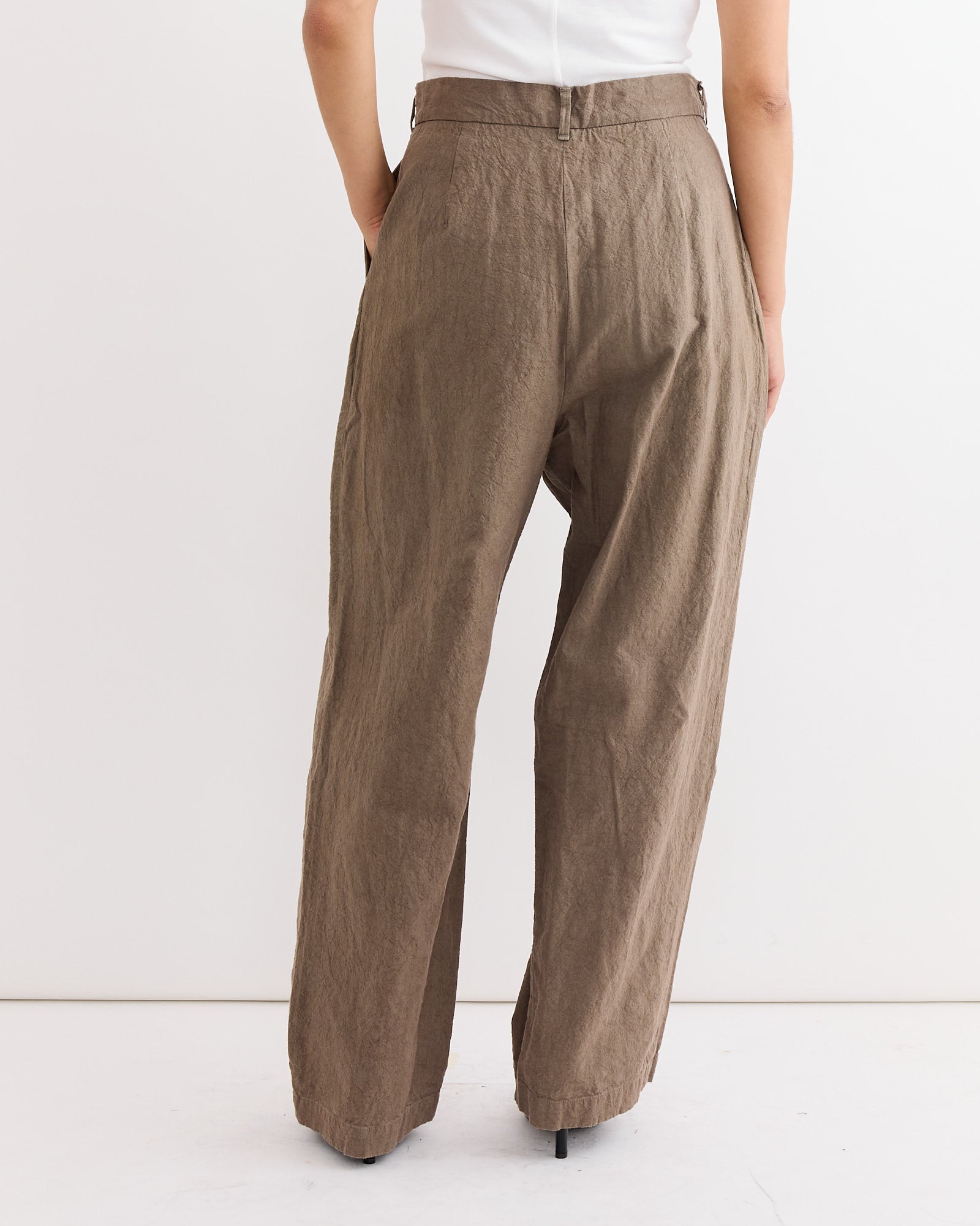 A person is shown from the back wearing Black Crane’s Crinkled Trouser in Khaki, styled high-waisted and loose-fitting, against a plain white background.