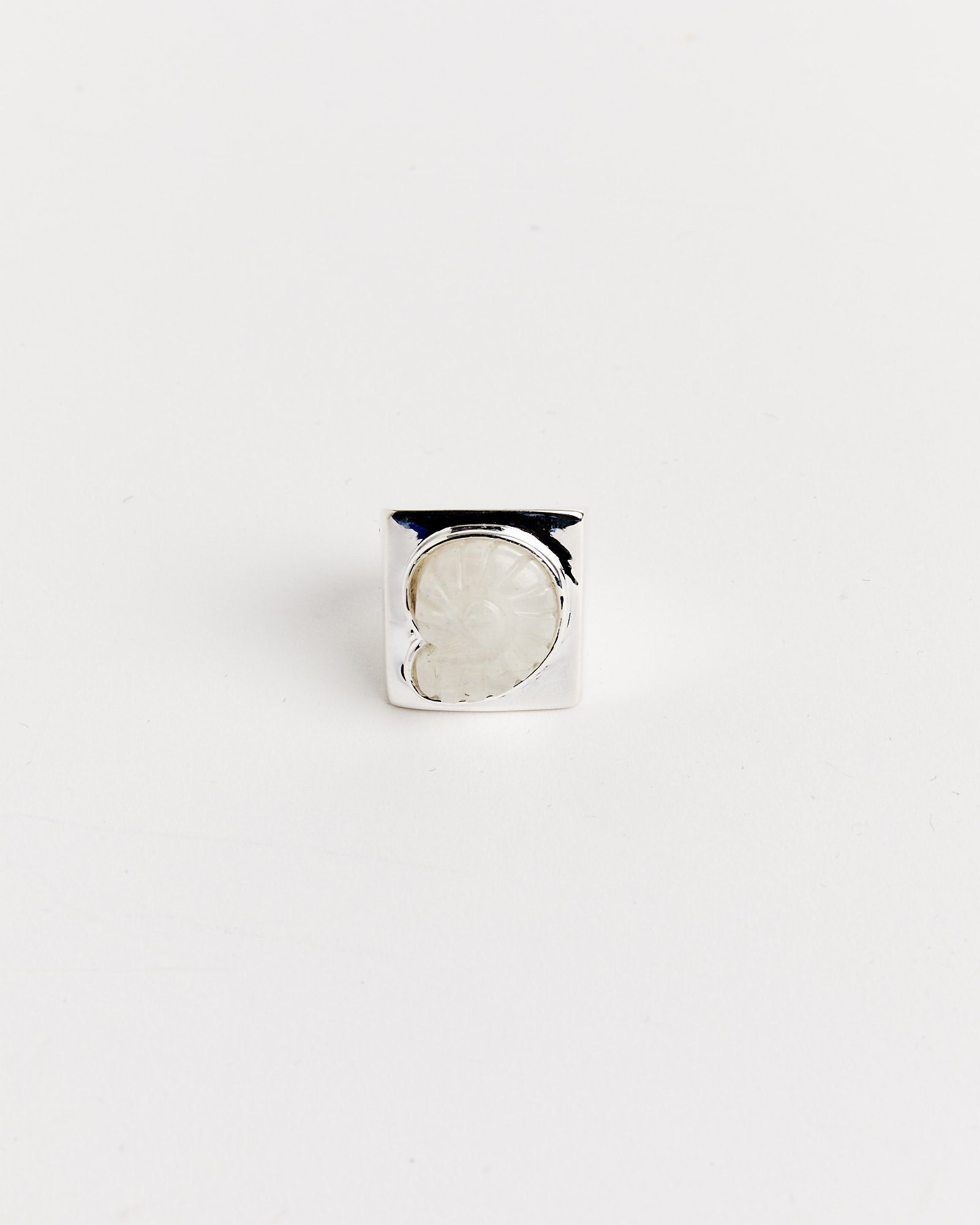 The Carved Nautilus Shell Ring by NOMIA features a square silver band with an oval white stone centerpiece, shown on a white background. Use our online chat for sizing advice and find your perfect fit.