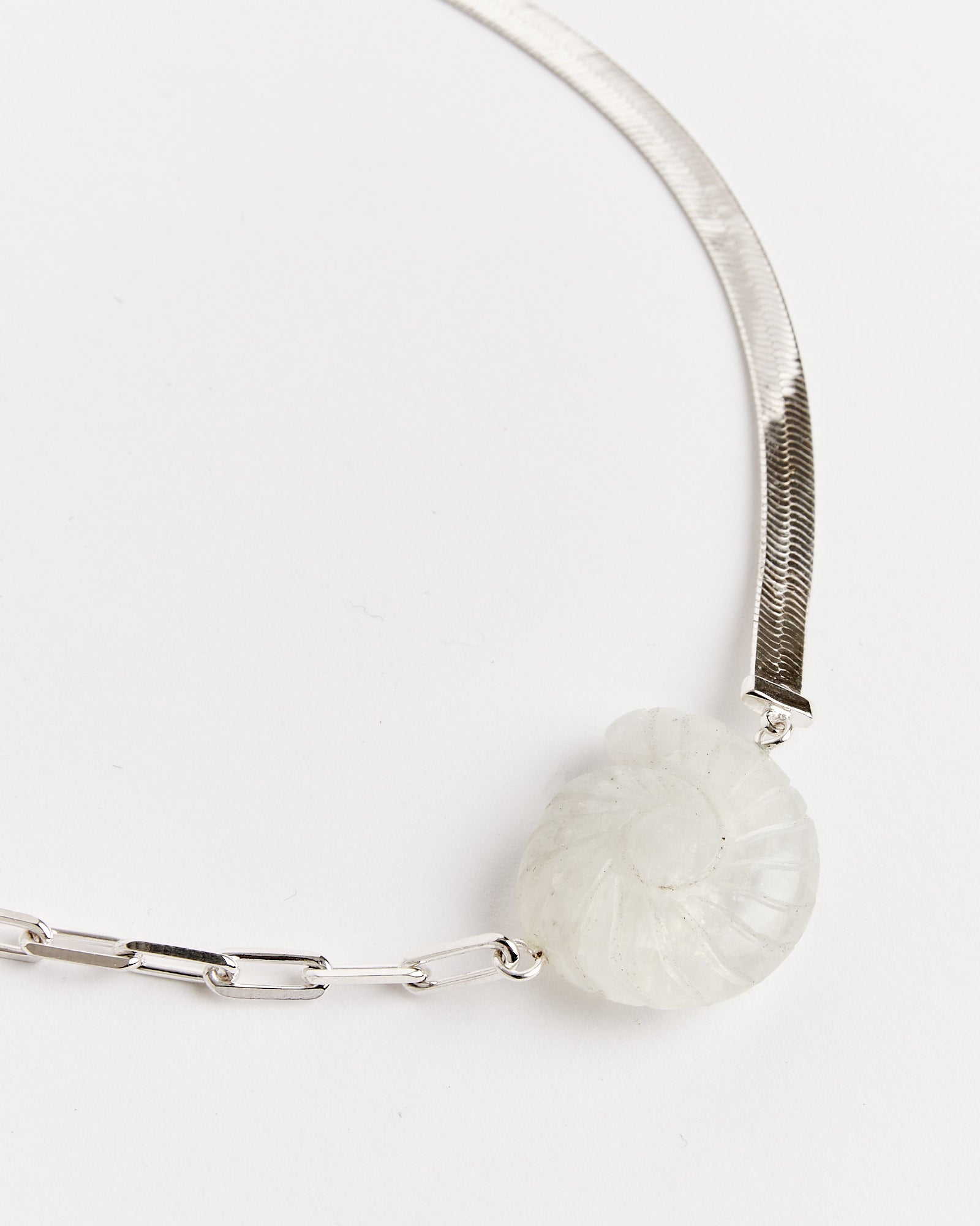 The NOMIA Crystal Shell Choker in Silver/Rainbow Moonstone features flat herringbone and chain links with a spiral, ammonite-inspired pendant. For fit or sizing questions, please use our online chat for assistance.