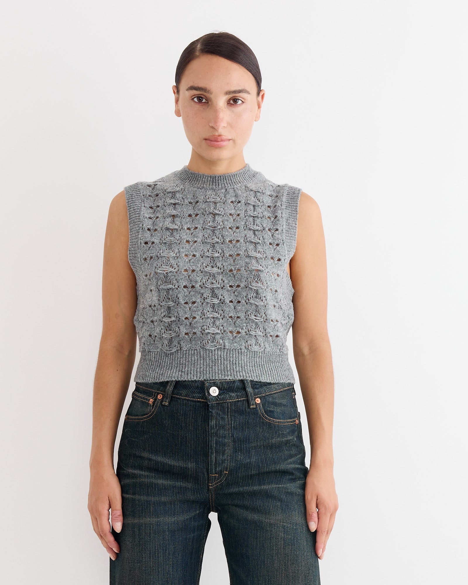 A woman with straight dark hair wears the Cecilie Bahnsen Brisa Vest in Light Grey and dark high-waisted jeans, standing against a plain white background and looking directly at the camera with a neutral expression.