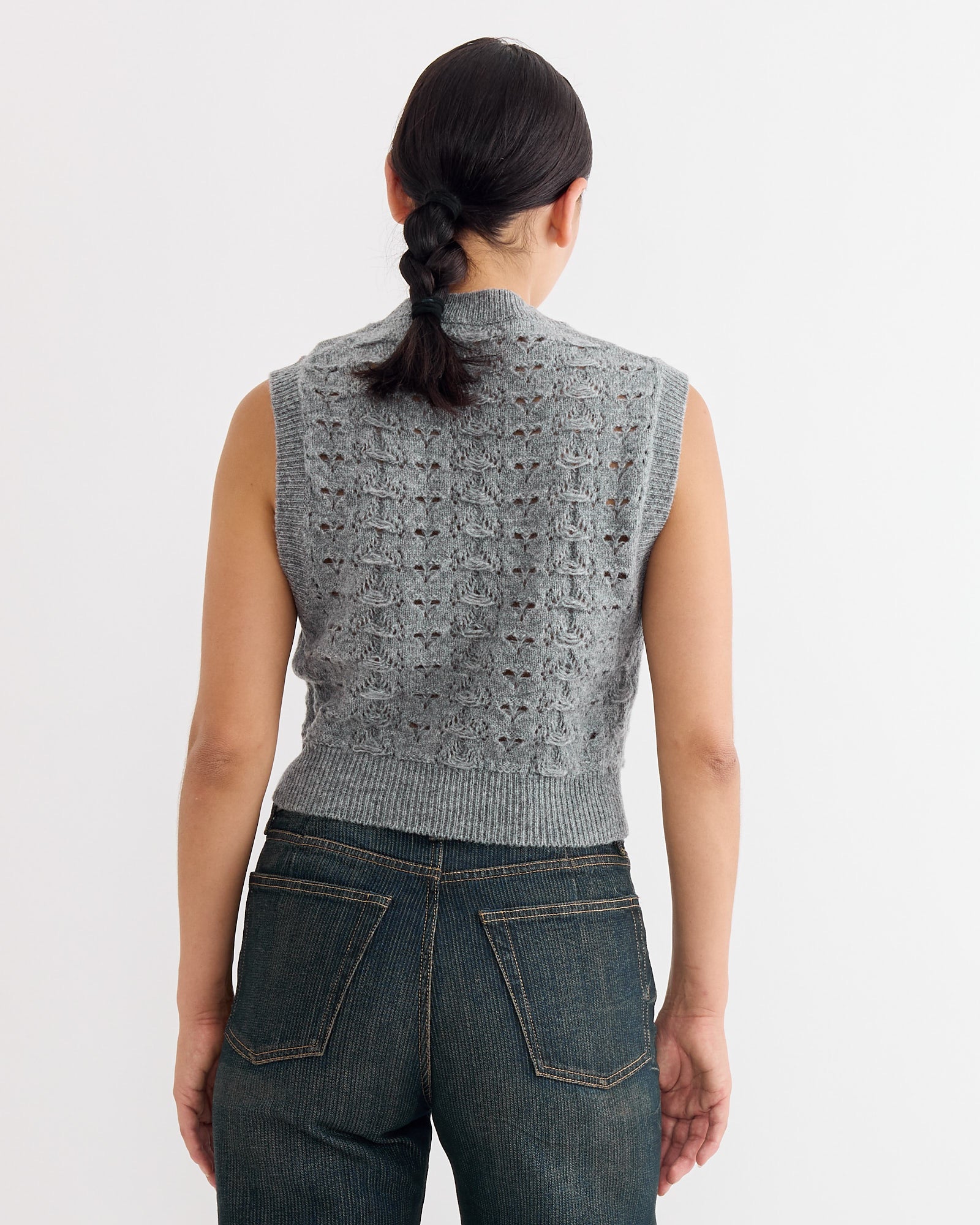 A person with dark braided hair is seen from the back, wearing the Cecilie Bahnsen Brisa Vest in Light Grey and dark blue jeans. For sizing or fit questions, use our online chat. Shown against a plain white background.